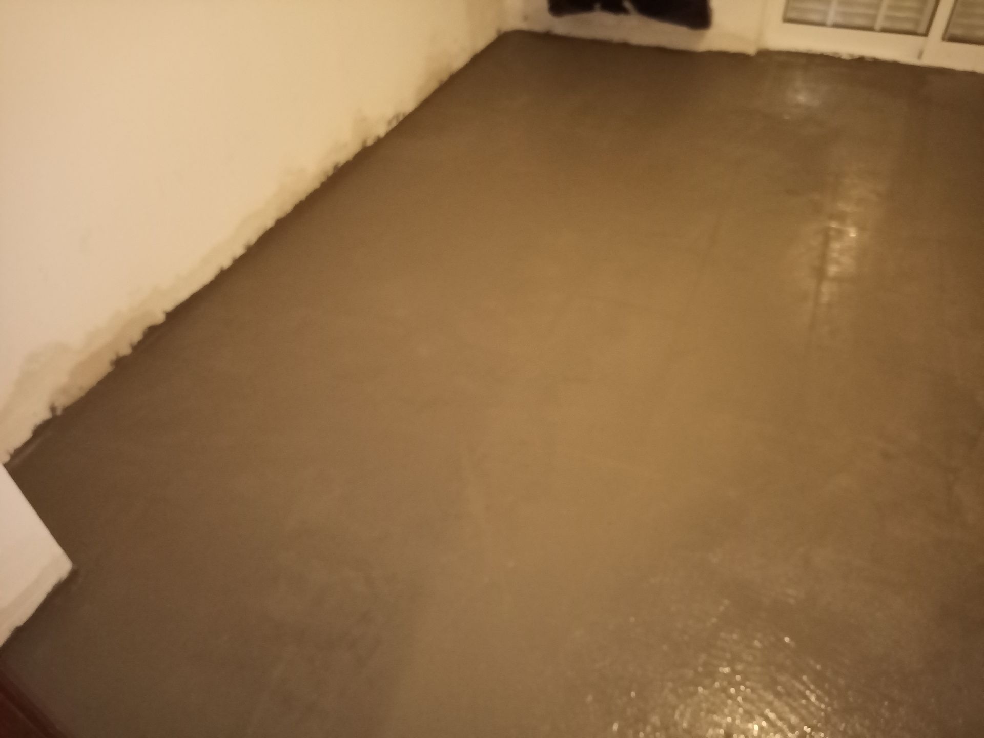 Piso de concreto recém-moldado em um cômodo, de cor marrom claro, com paredes laterais.