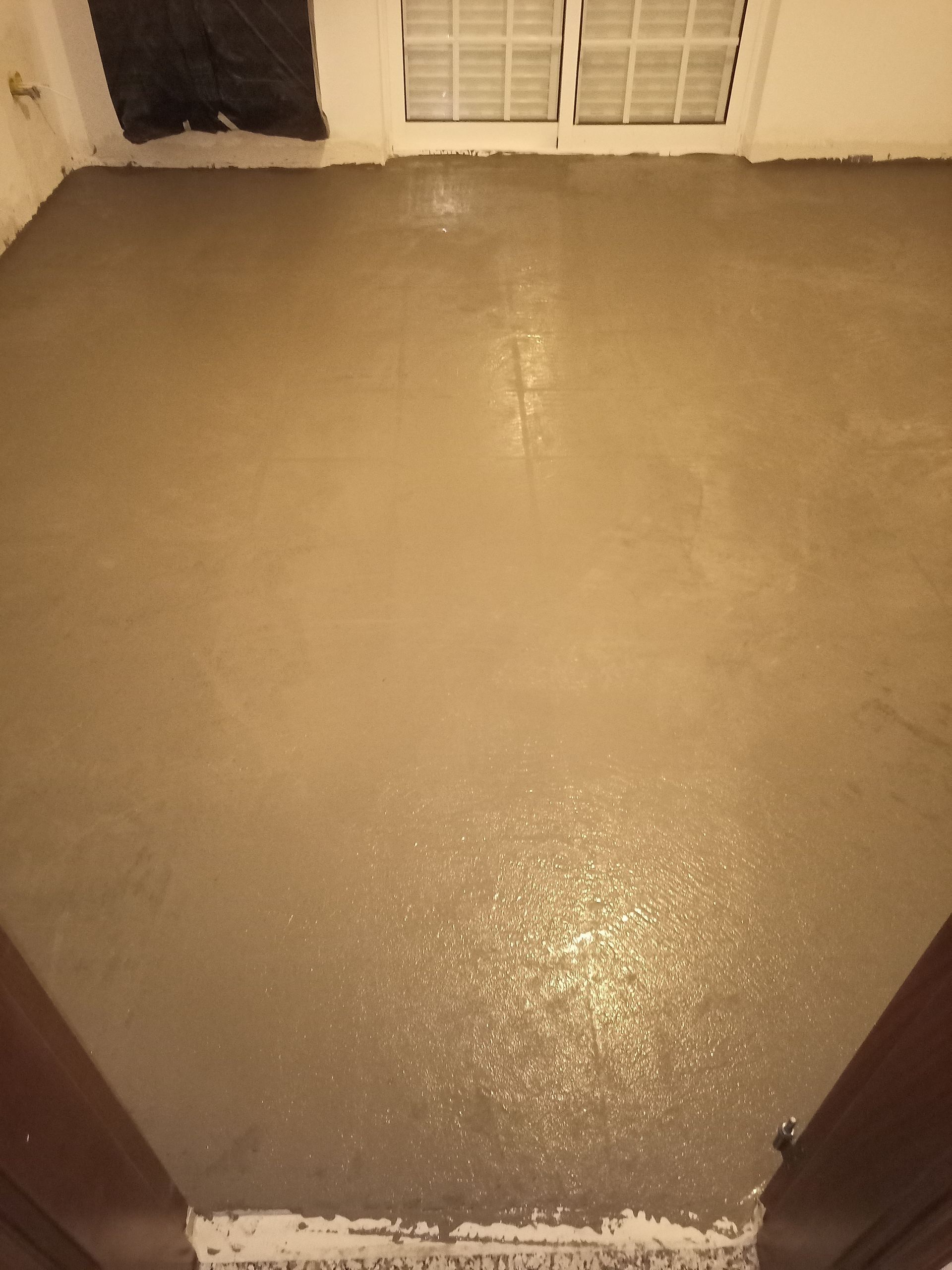 Piso de concreto recém-moldado em um cômodo, com a moldura da porta visível na parte inferior.