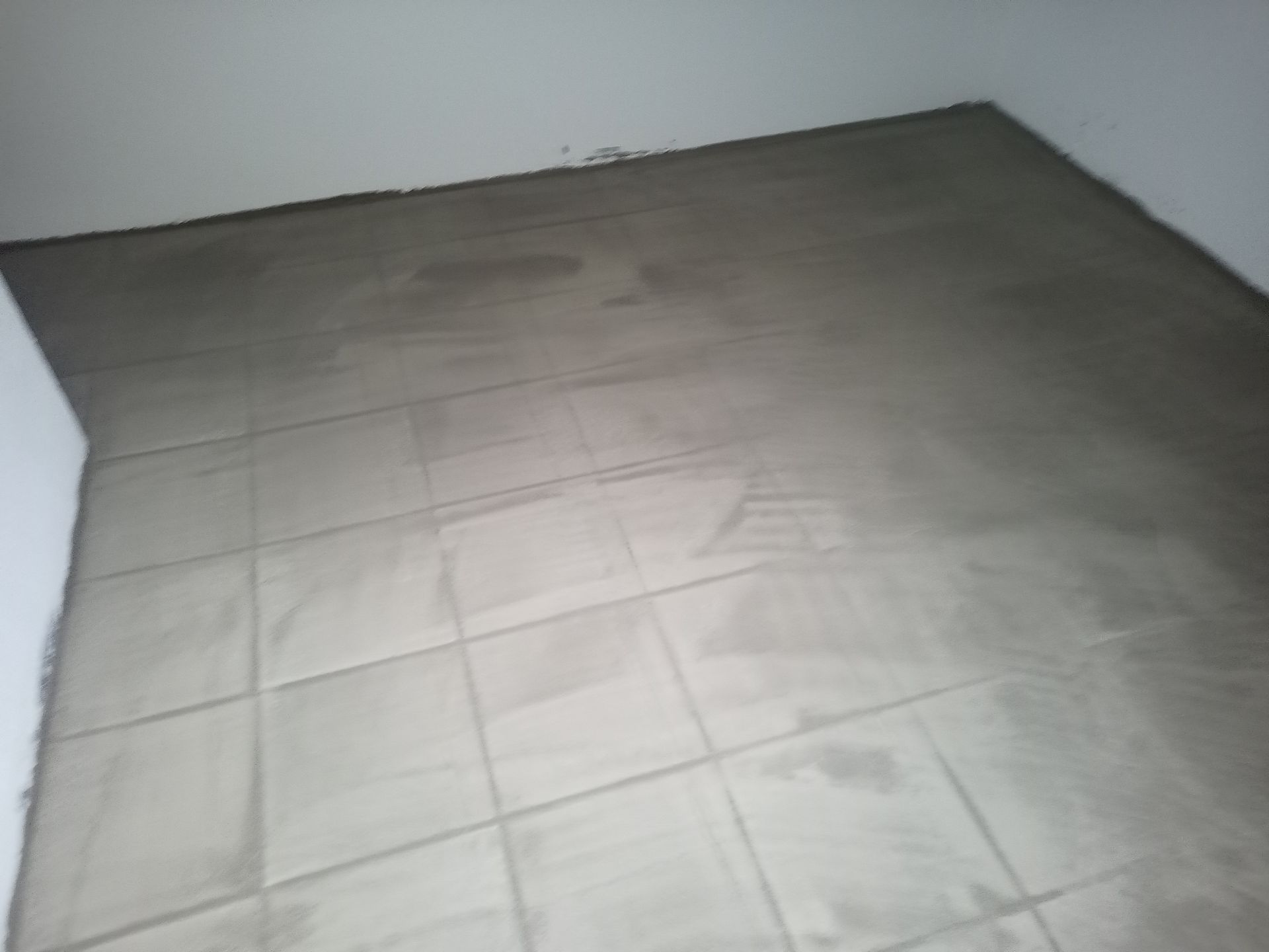 Piso de azulejos cinza no canto de uma sala, com uma parede branca parcialmente visível.