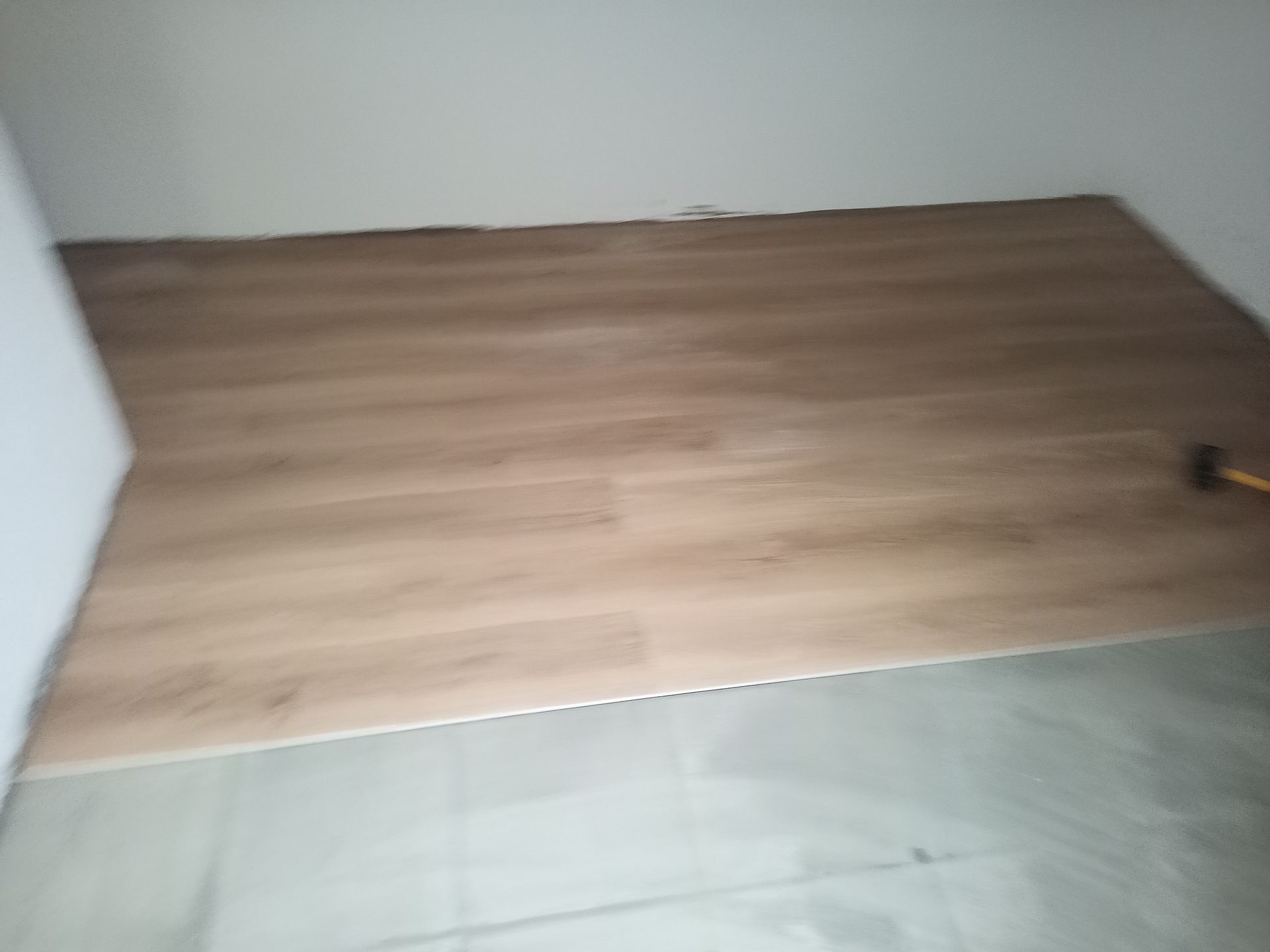 Instalação de piso laminado em um piso adjacente a uma parede branca. O piso existente está visível.