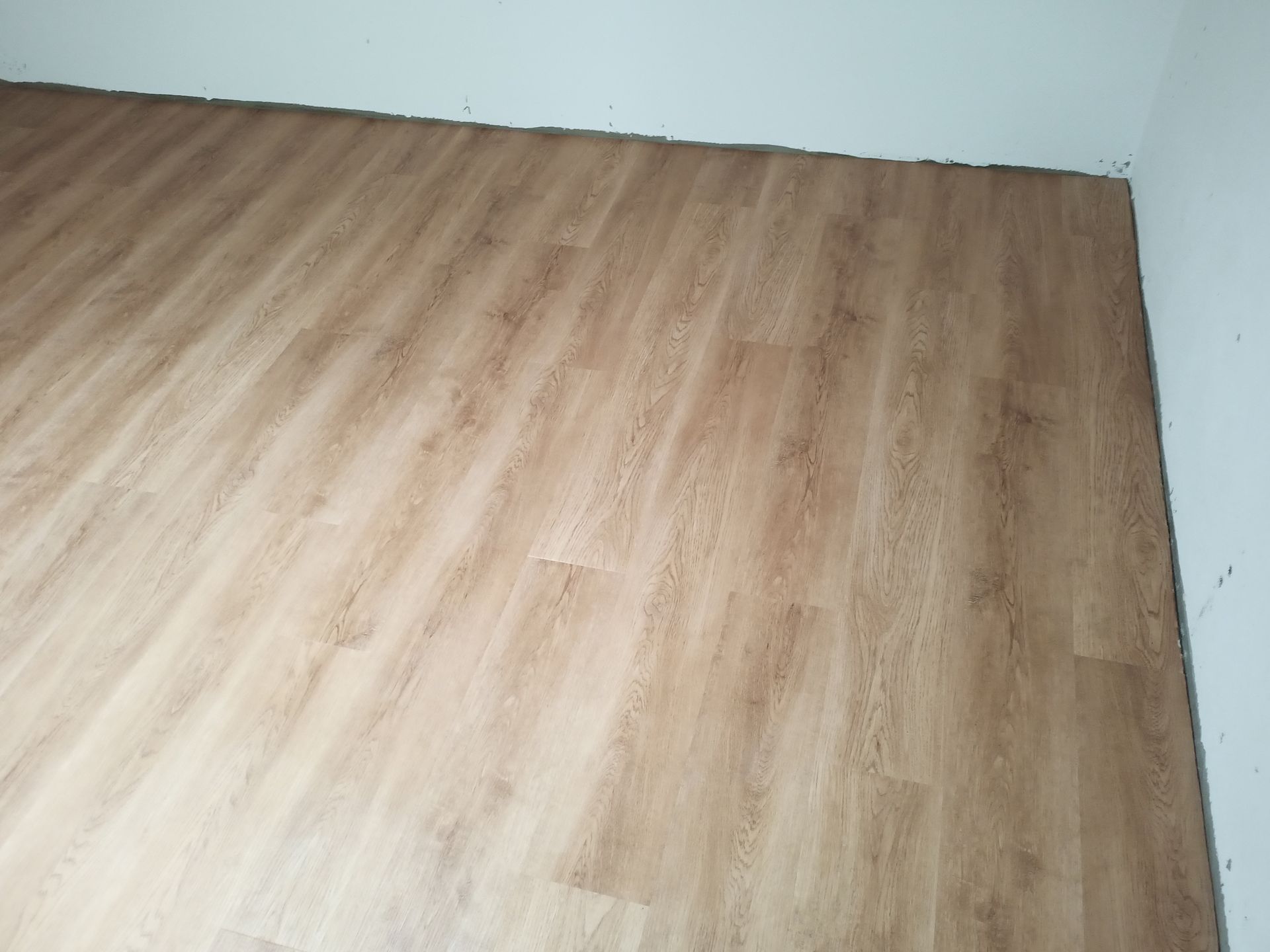 Piso imitando madeira em tom castanho claro instalado em um cômodo com paredes brancas.