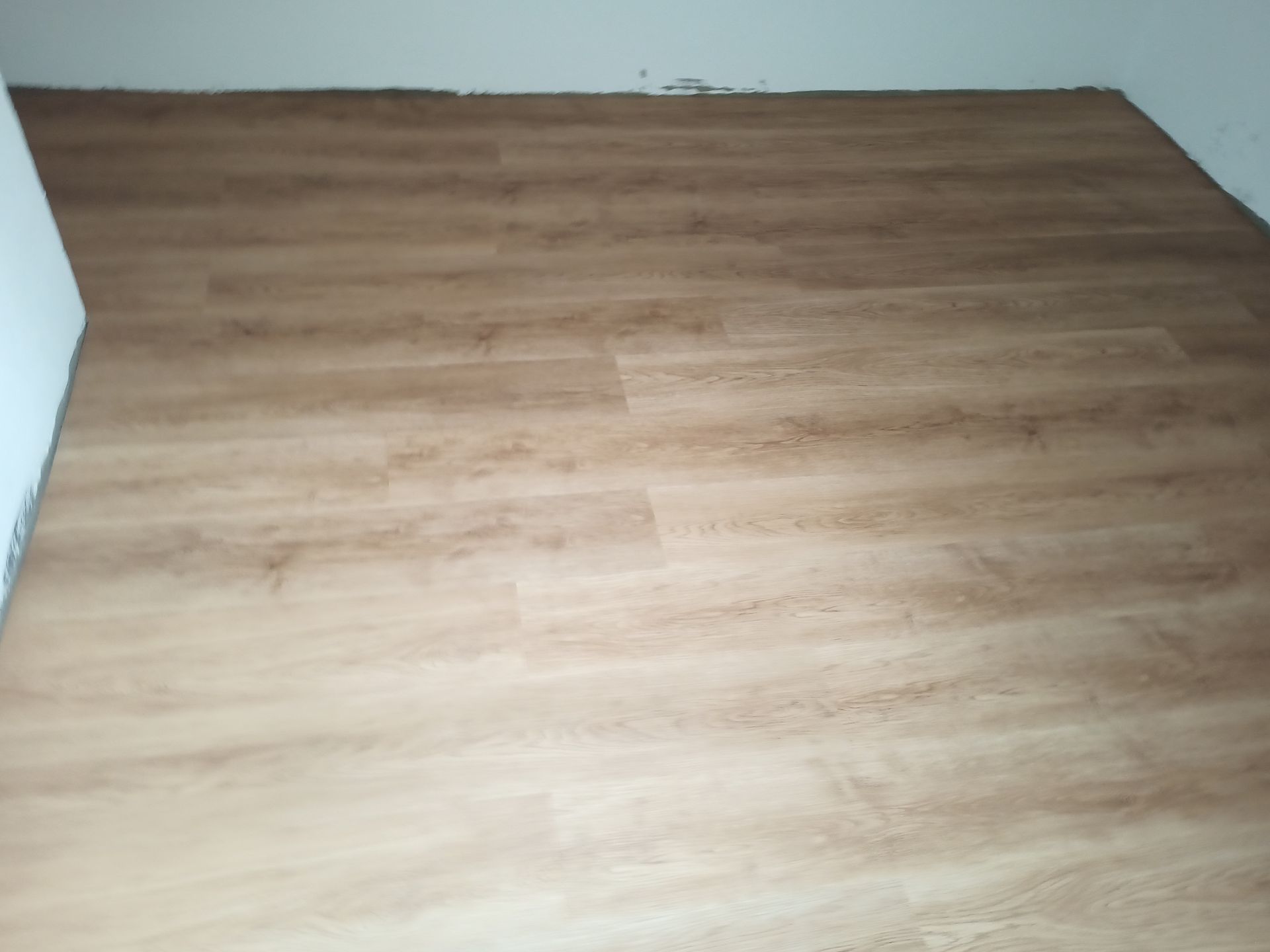 Piso laminado com aparência de madeira instalado em um cômodo, encontrando as paredes brancas no perímetro.