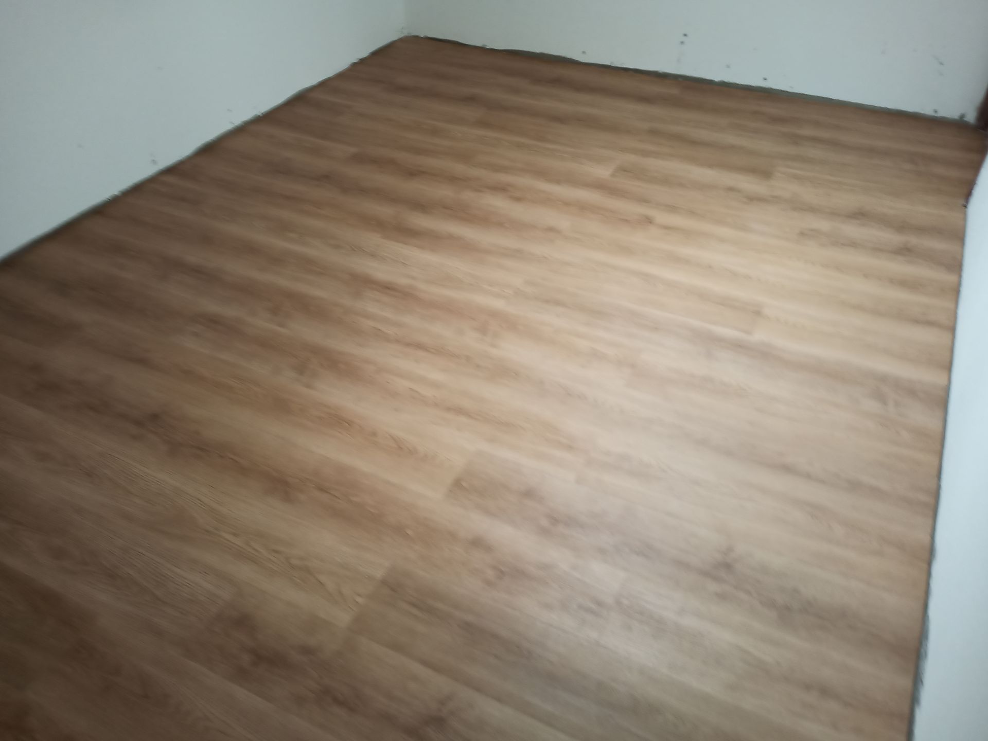 Piso com aparência de madeira em uma sala com paredes brancas, vista de baixo para cima.