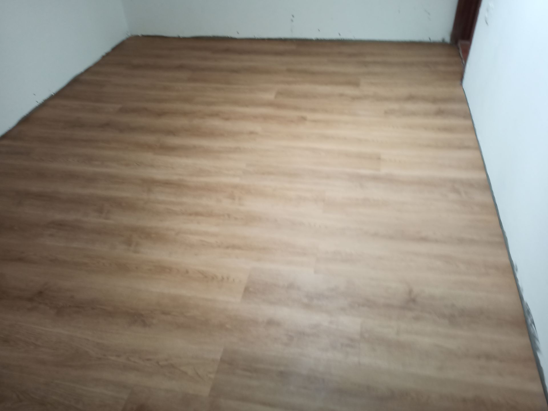 Piso de madeira instalado em um cômodo com paredes brancas e cantos visíveis.