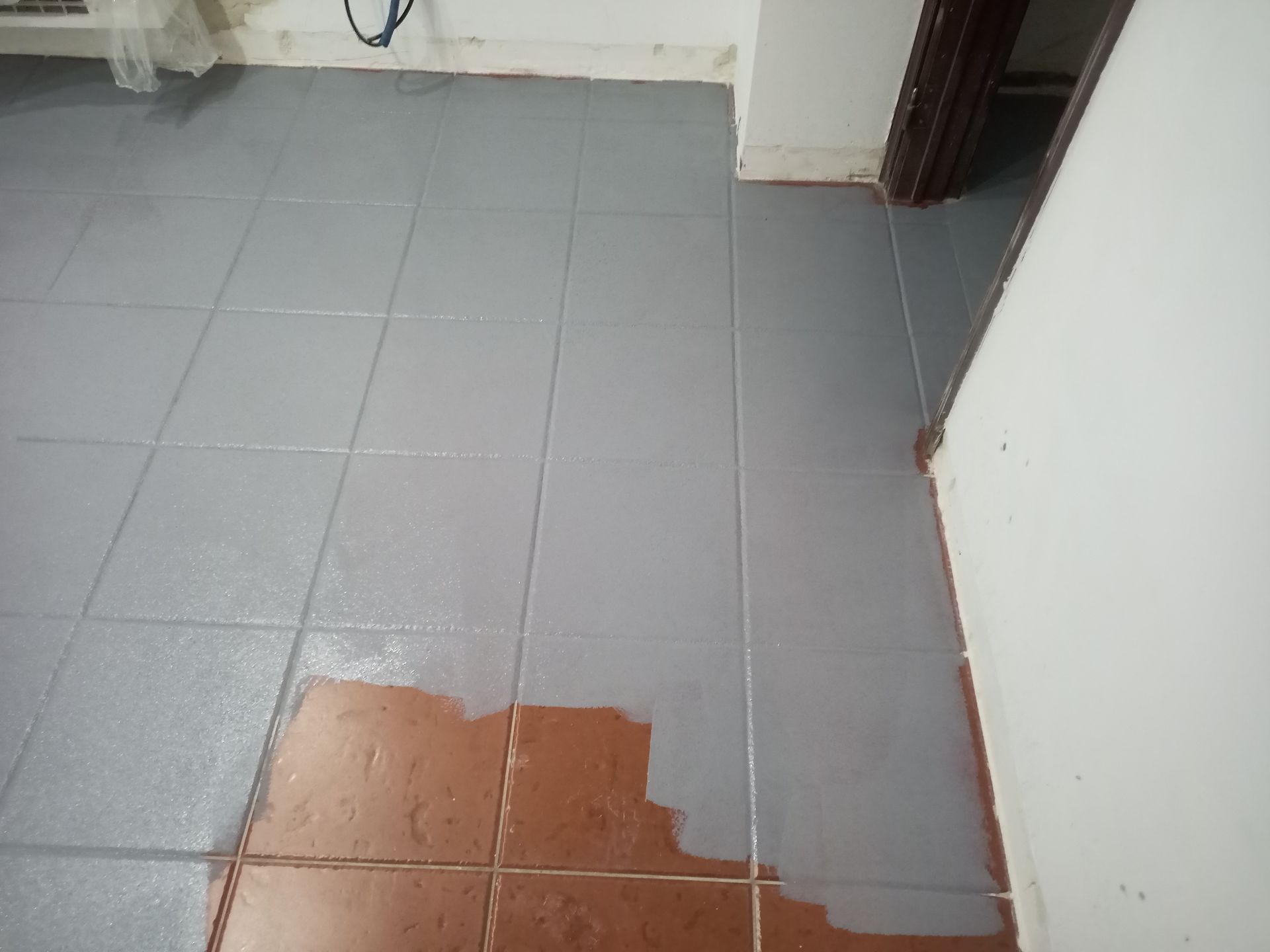 Piso de azulejos pintados de cinza com azulejos marrons sem pintura à mostra.