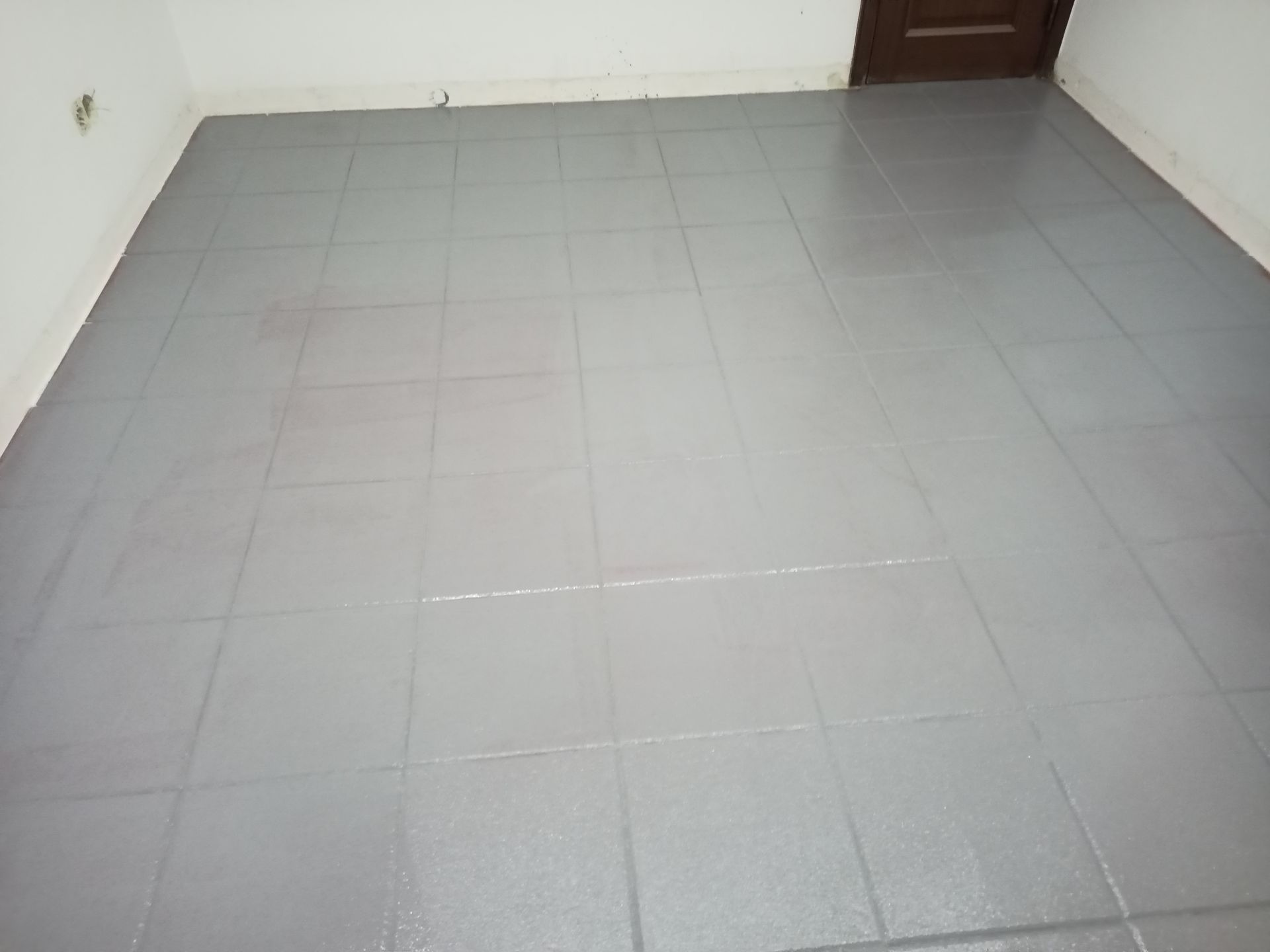 Piso de azulejos pintado de cinza em um cômodo, com a porta ao fundo.