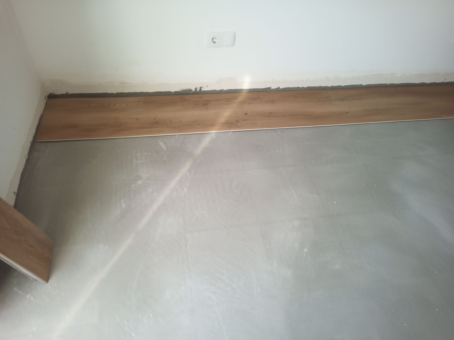 Um close-up de um piso imitando madeira parcialmente instalado contra uma parede branca.