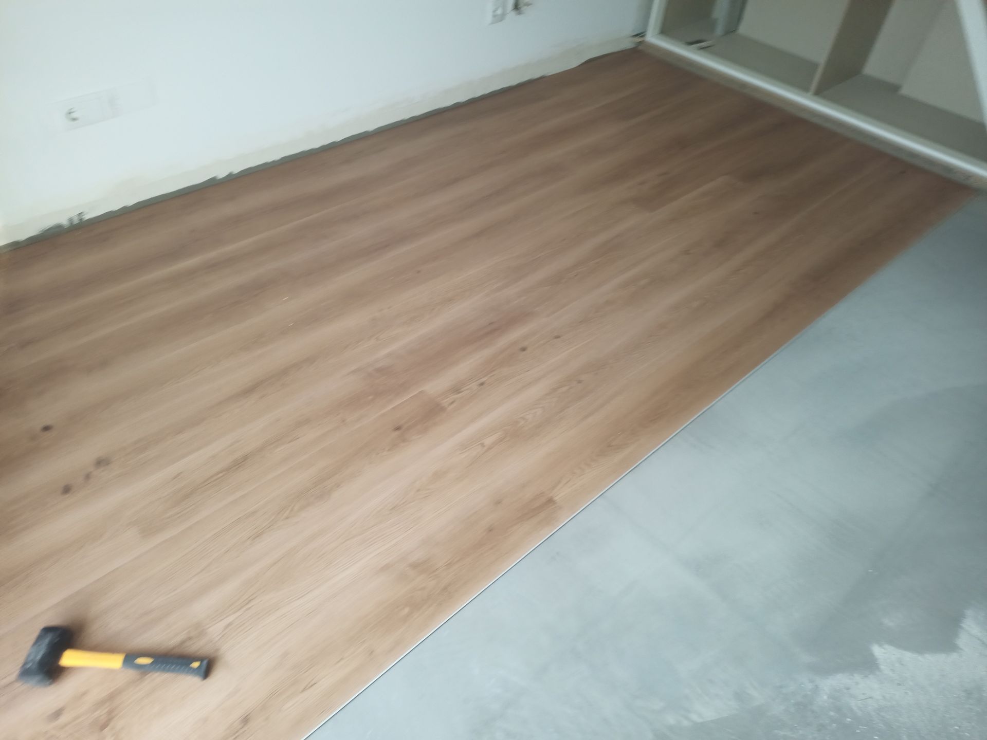 Piso com aparência de madeira sendo instalado em um cômodo, martelo no chão.