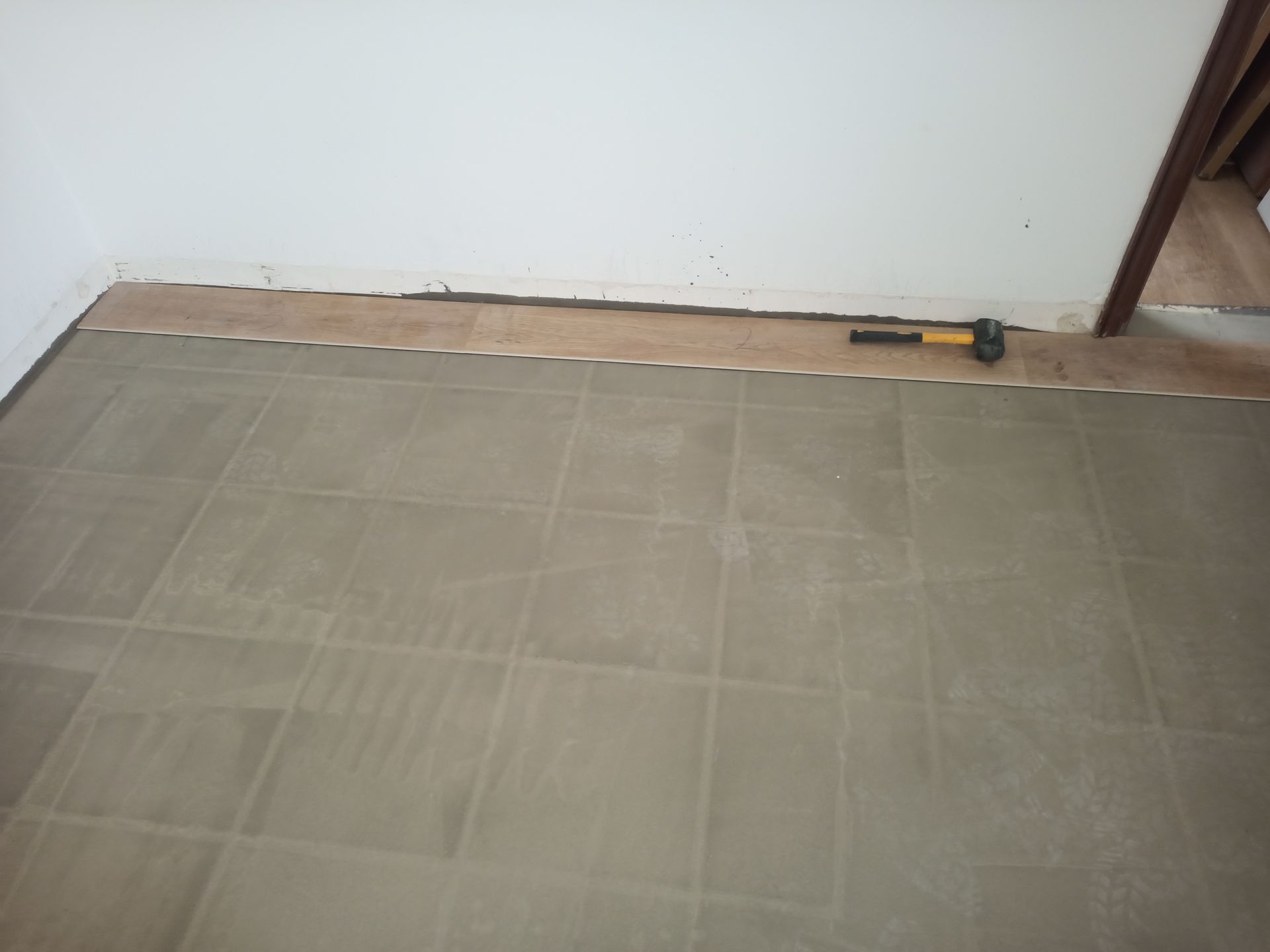 Piso com azulejos instalados, piso inacabado encostado na parede, martelo em cima.