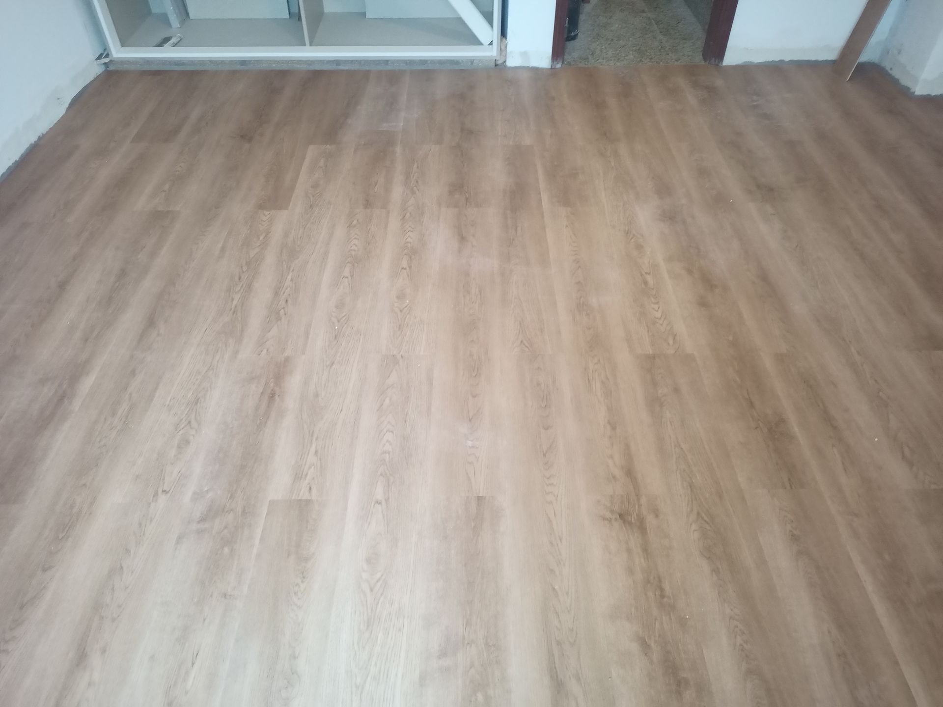 O piso laminado com aparência de madeira se estende da parte inferior da imagem até o meio. Ao fundo, vê-se um armário branco.