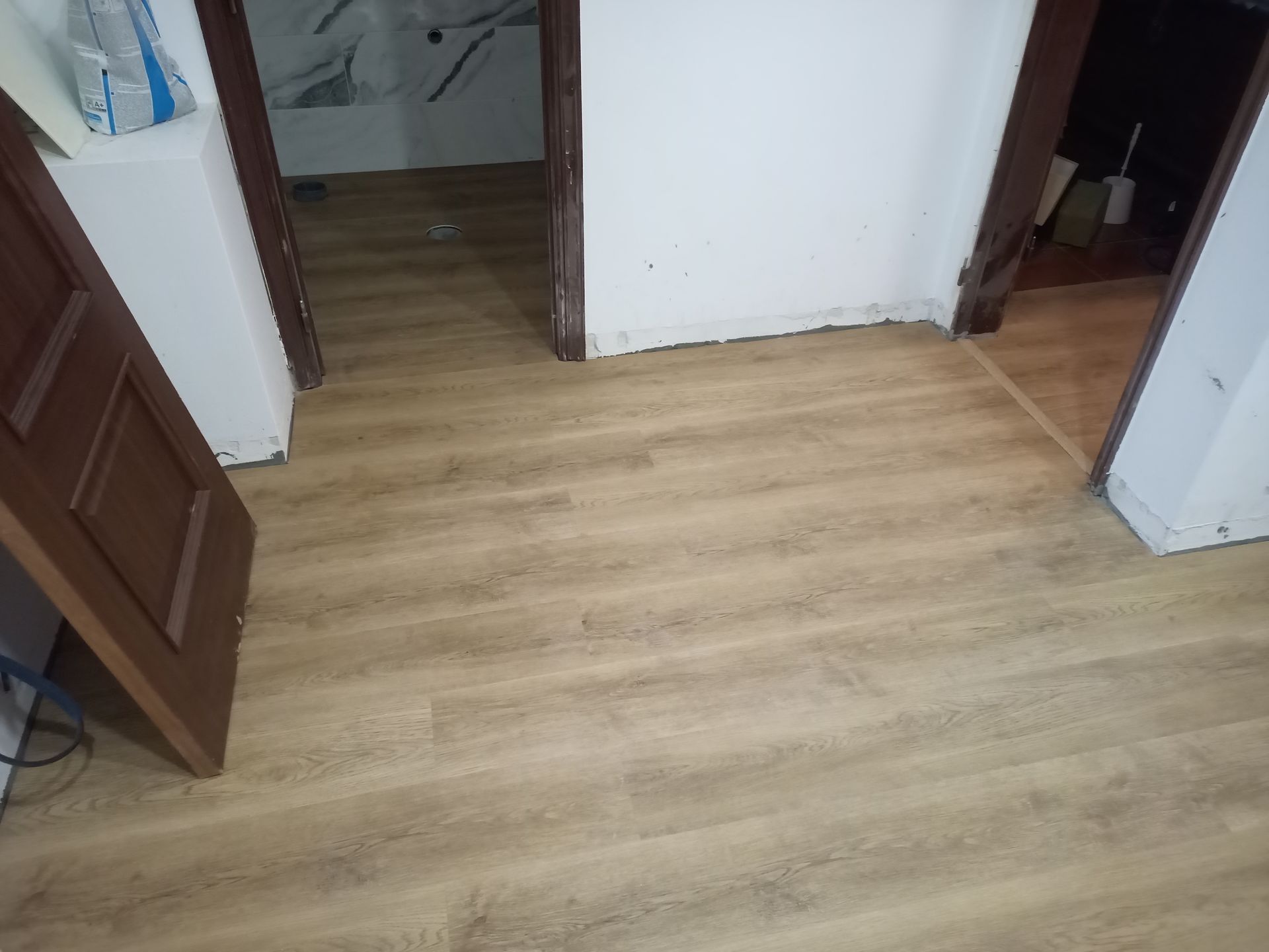 Piso imitando madeira em tom castanho claro instalado em um corredor com portas em ambos os lados.