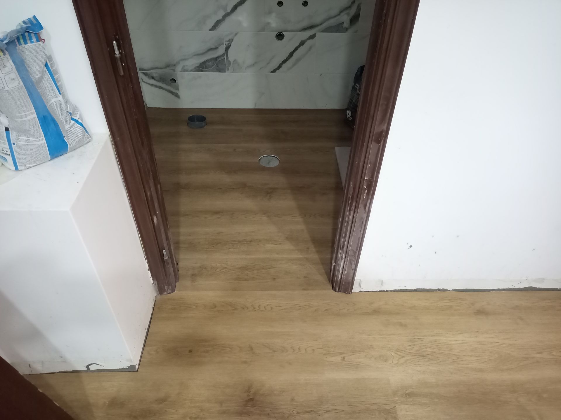 Porta aberta com moldura de madeira marrom e piso marrom claro; vista interior.