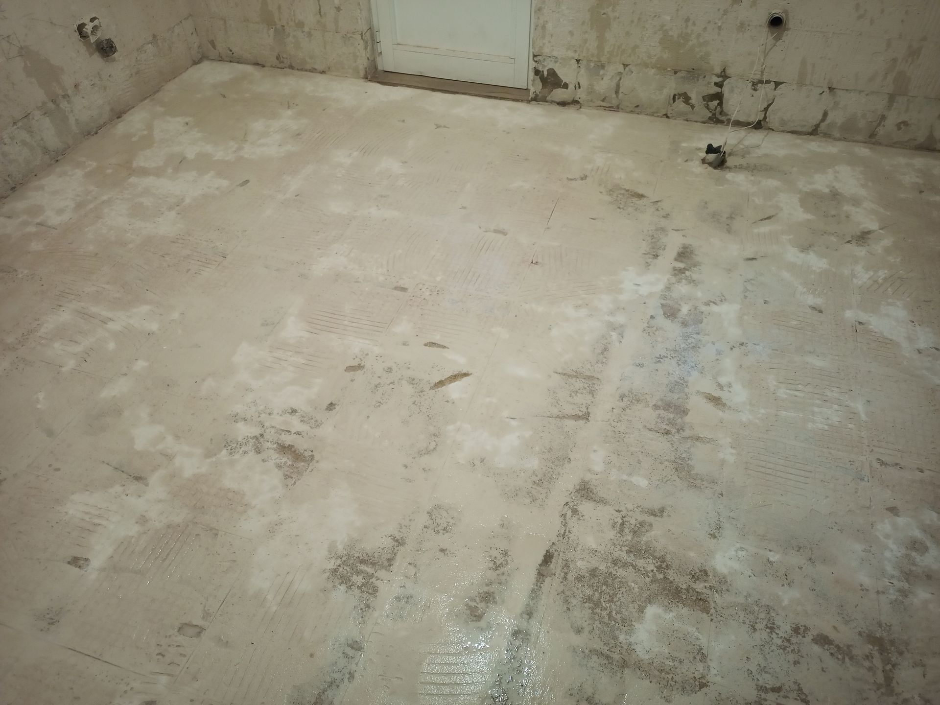 Piso de cimento aparente em um cômodo em construção, com remendos visíveis e textura áspera.