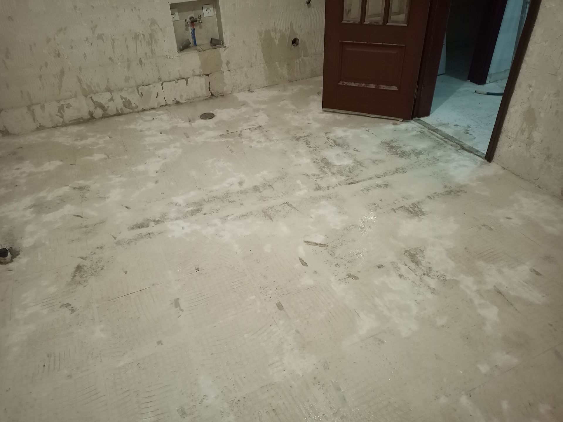 Quarto com piso de concreto bruto, porta marrom e paredes inacabadas.
