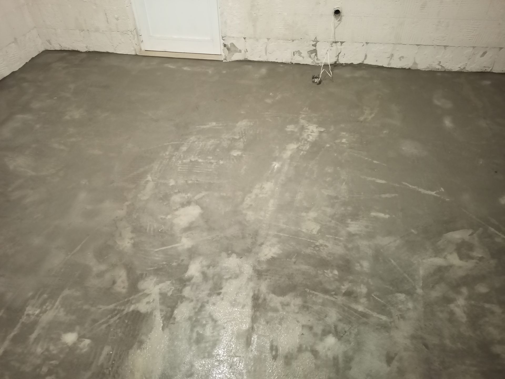 Piso de cimento cinza recém-lançado em um cômodo, com marcas visíveis da desempenadeira e alguns pontos de água acumulada.