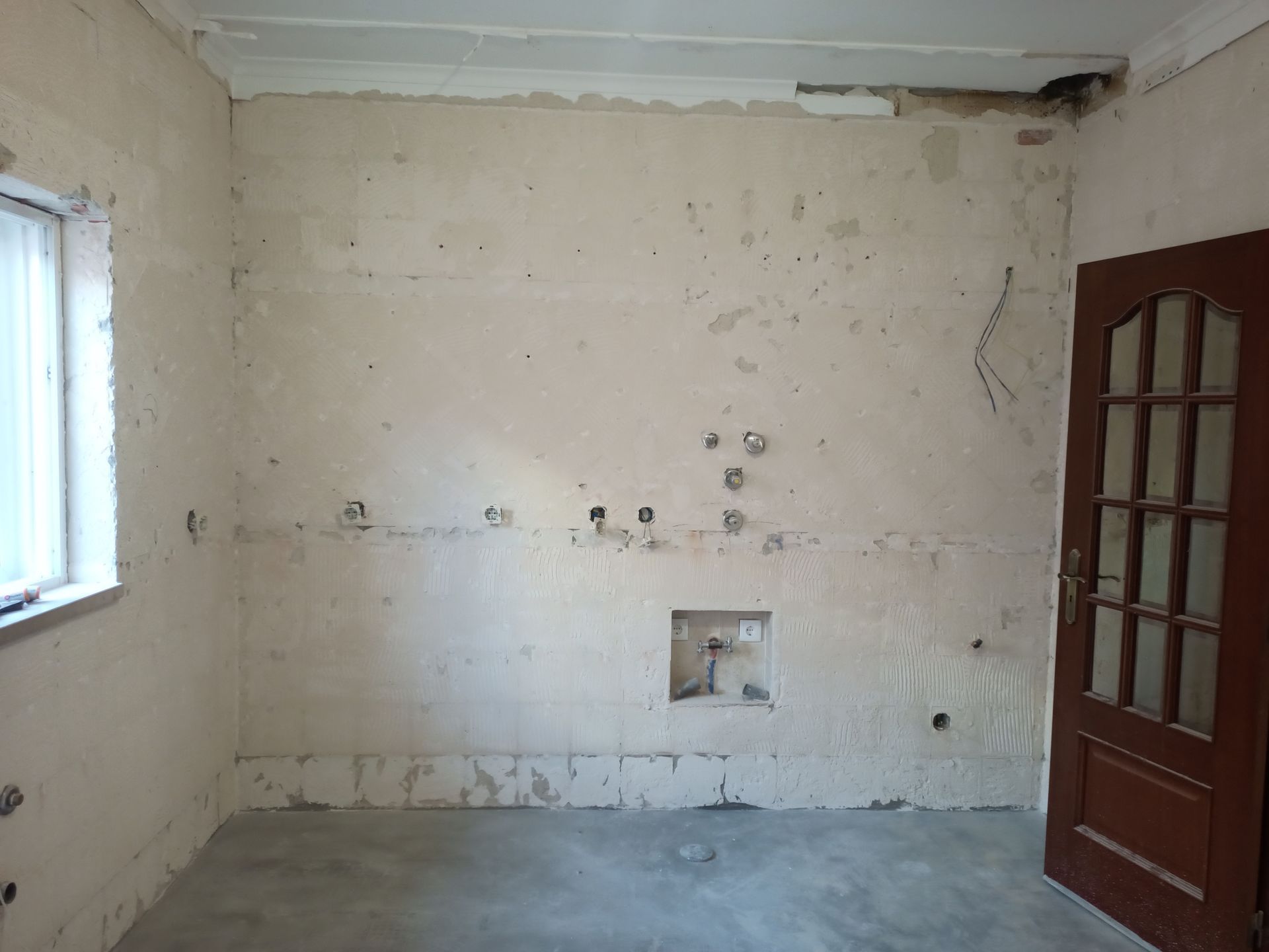 Paredes da cozinha nuas, com tomadas elétricas e uma porta, preparadas para reforma.