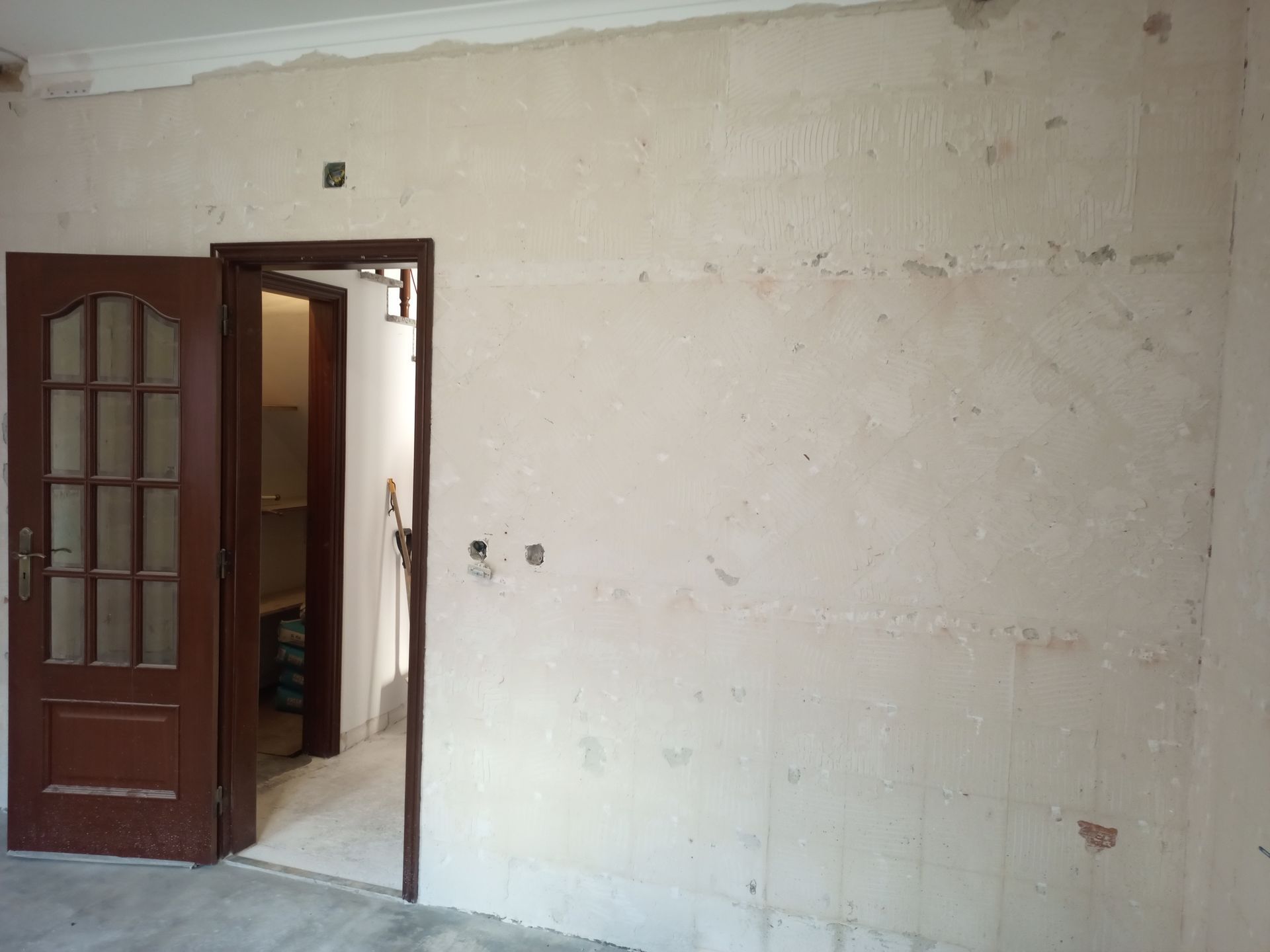 Vista interior de um cômodo com portas marrons, entrada aberta e paredes inacabadas.