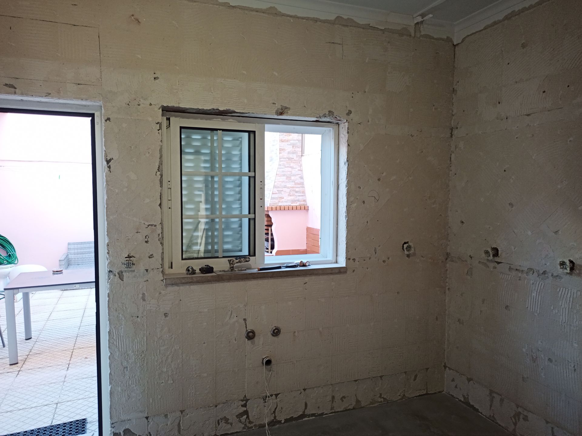 Reforma de cômodo interno com paredes expostas, janela e porta para o pátio.