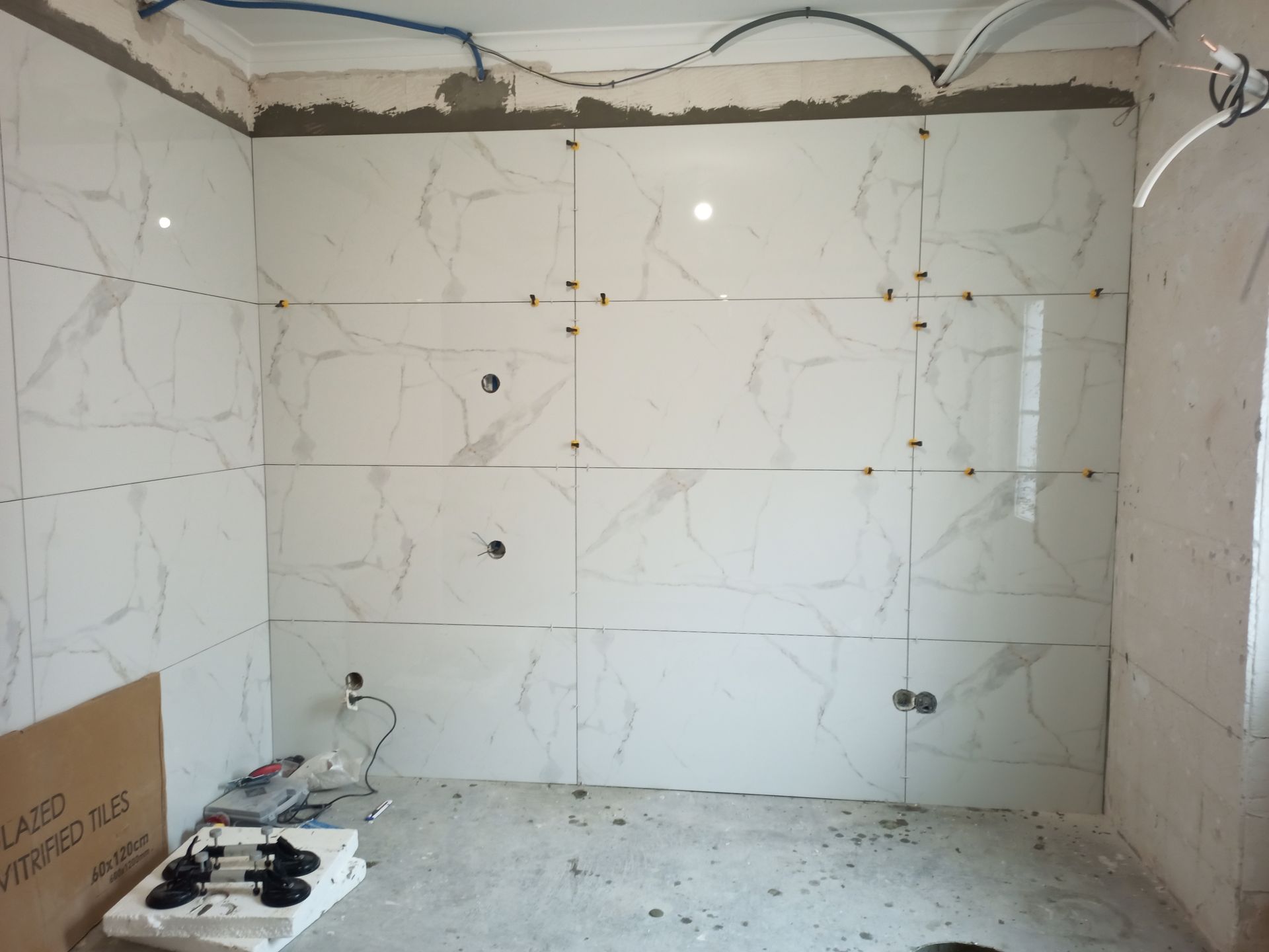 Paredes do banheiro parcialmente revestidas com azulejos brancos que imitam mármore; obra em andamento.