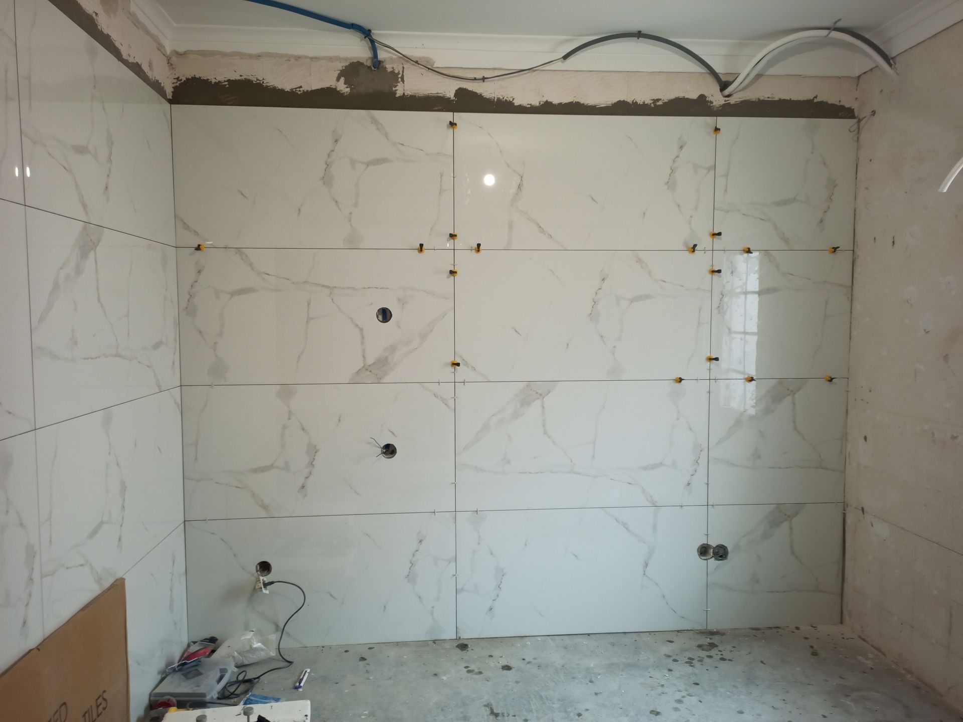 Azulejos de mármore branco sendo instalados em uma parede da cozinha, com espaçadores no lugar.