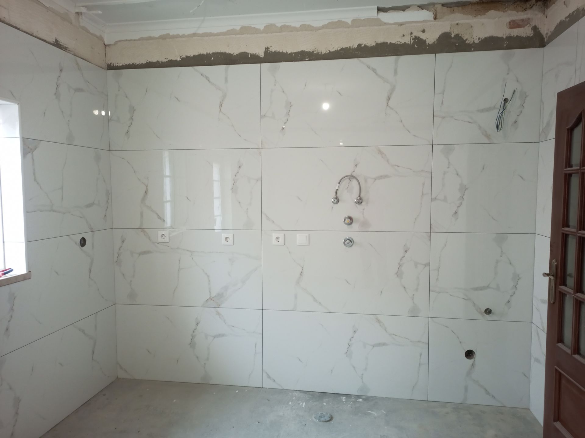 Banheiro em reforma com azulejos brancos imitando mármore nas paredes e uma torneira parcialmente instalada.