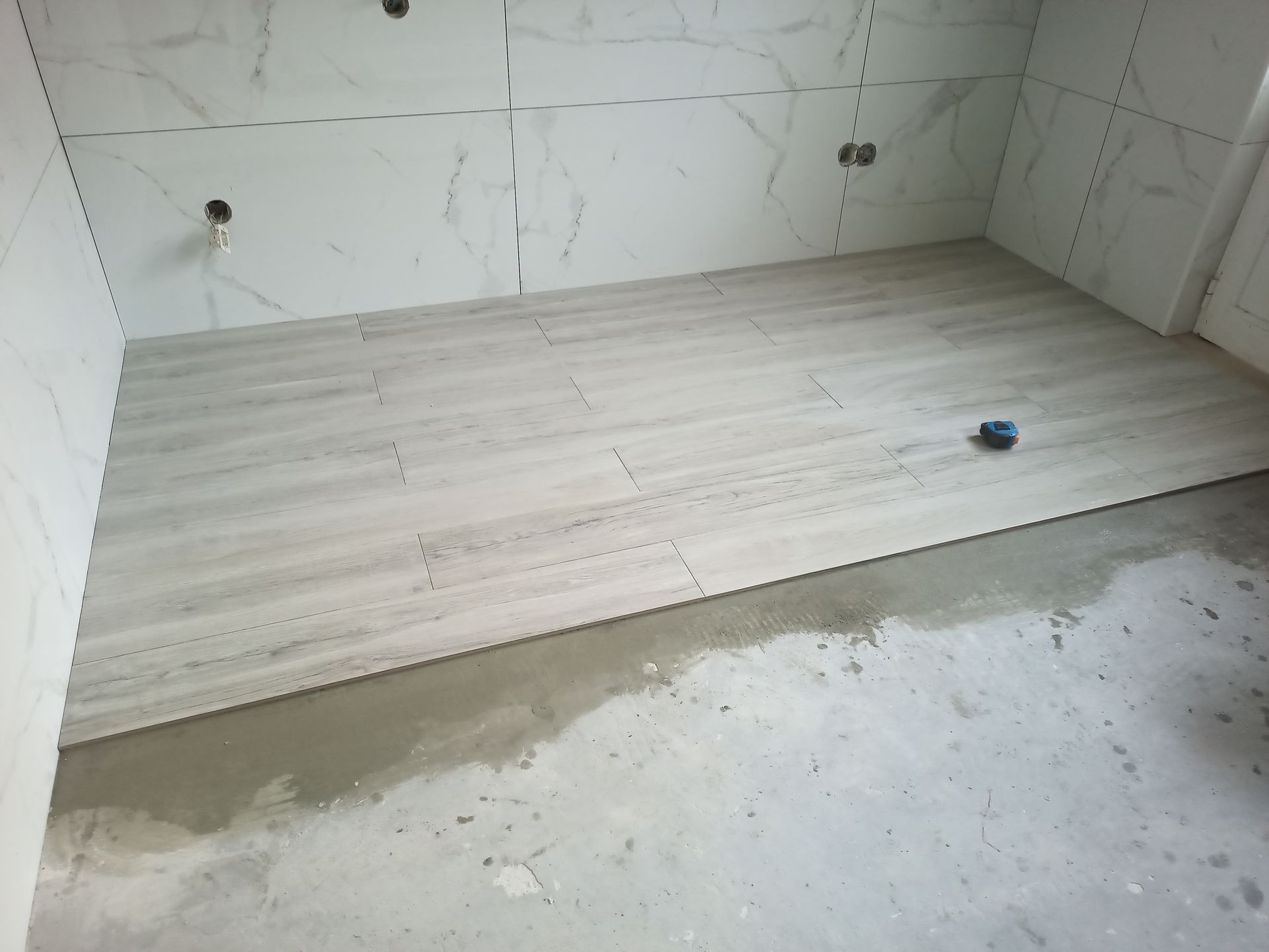 Quarto interior com piso parcialmente revestido com ladrilhos cinza; azulejos brancos nas paredes; piso de concreto aparente.