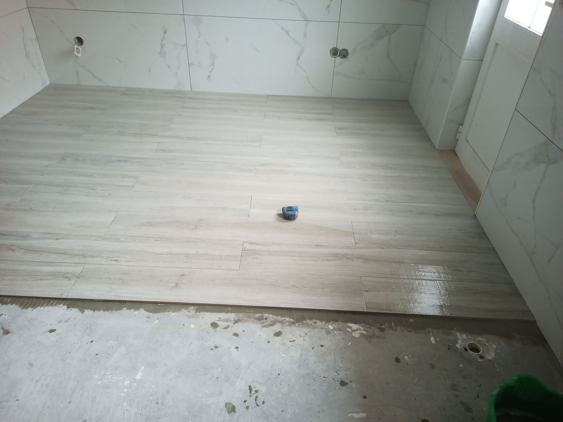 Banheiro com instalação de piso novo em andamento; paredes revestidas com azulejos; cimento fresco.