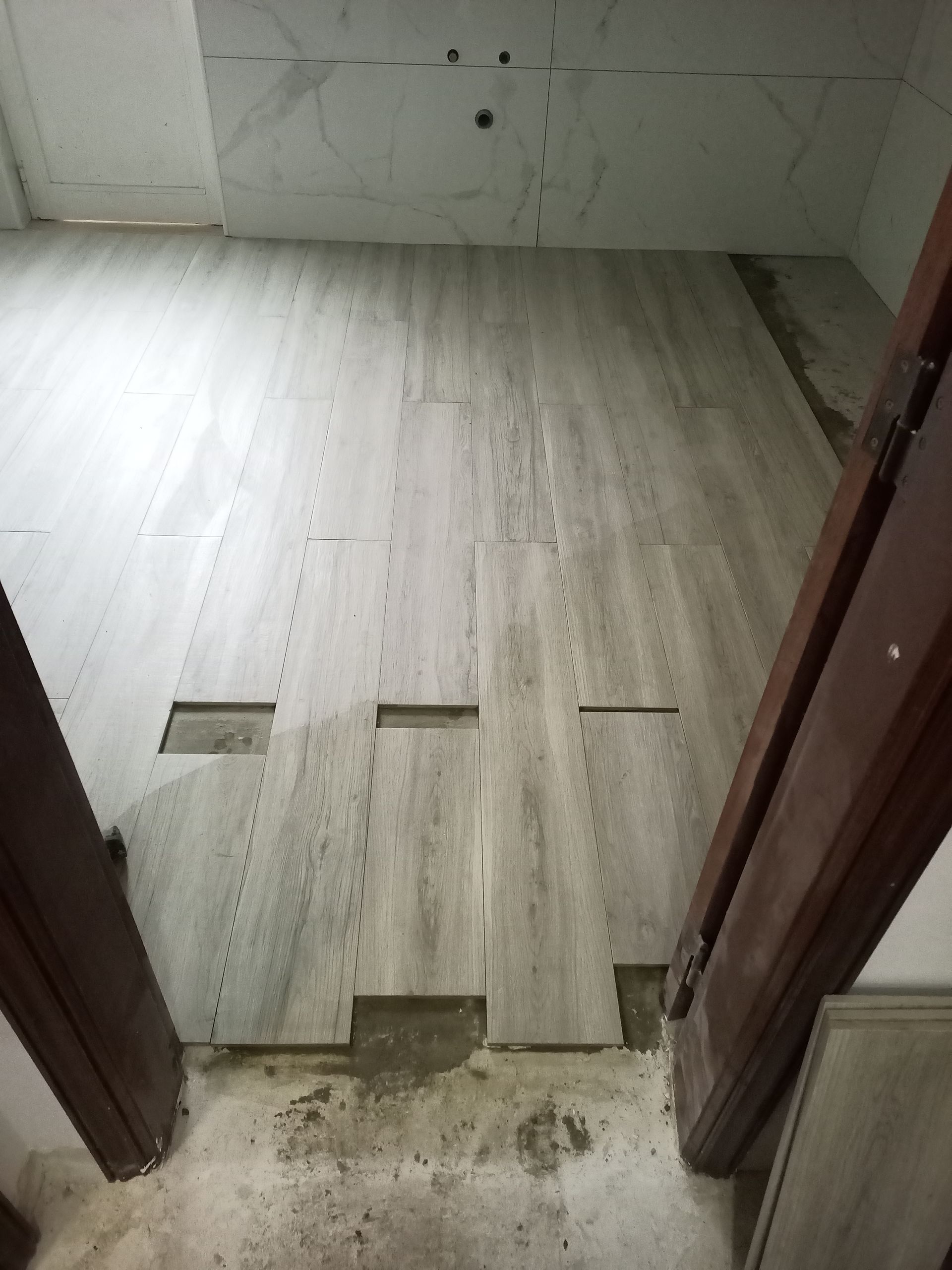 Instalação de piso de cerâmica cinza claro, com batentes de portas à vista.