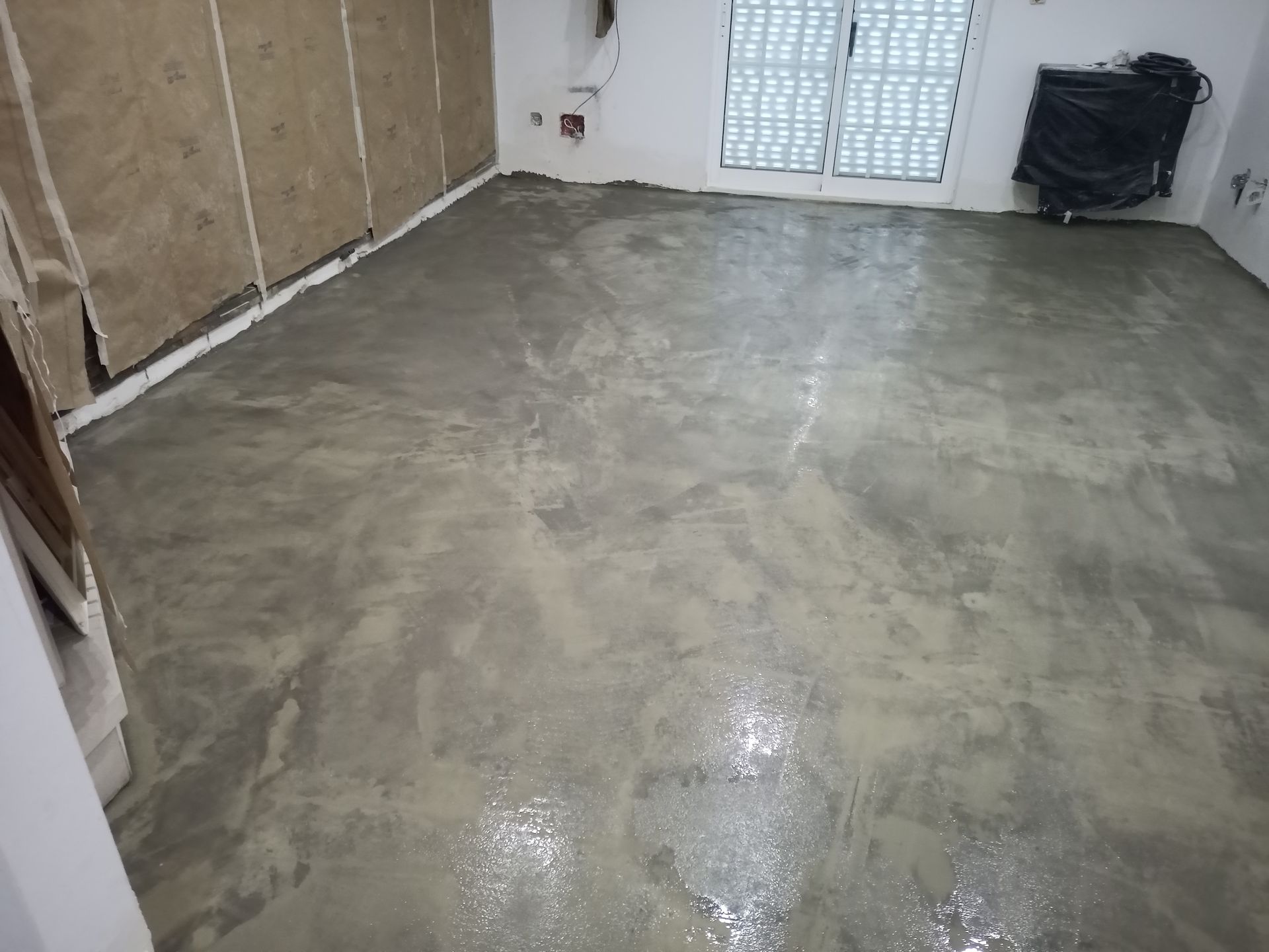Piso de concreto cinza recém-moldado em um cômodo com paredes nuas e janela fechada.