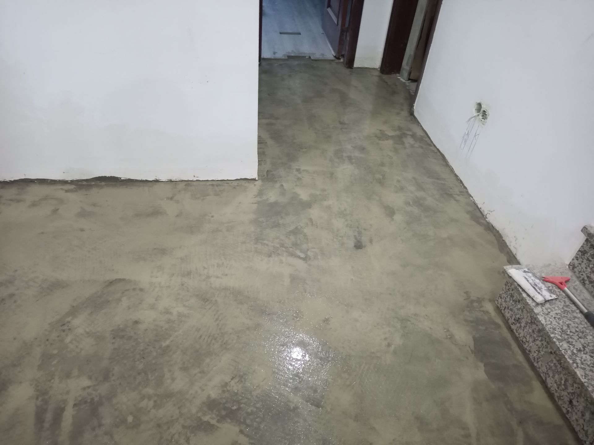 Piso de concreto em um corredor, recém-moldado e ainda úmido, com paredes brancas e vislumbre de outros cômodos.