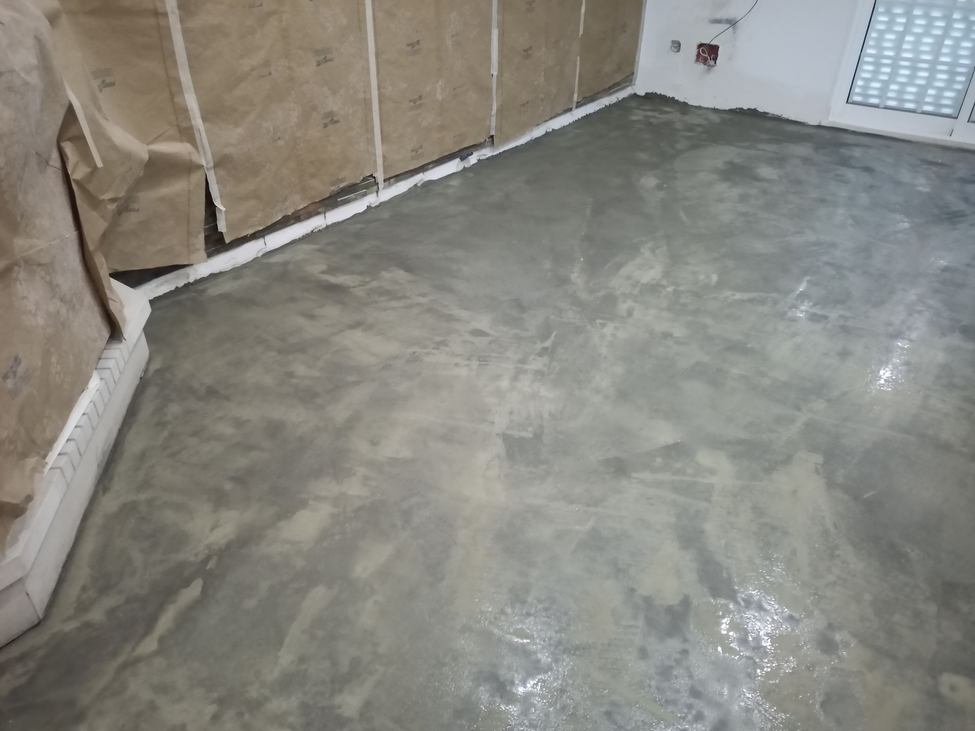 Piso de concreto sendo instalado em um cômodo, com papel pardo protegendo as paredes.