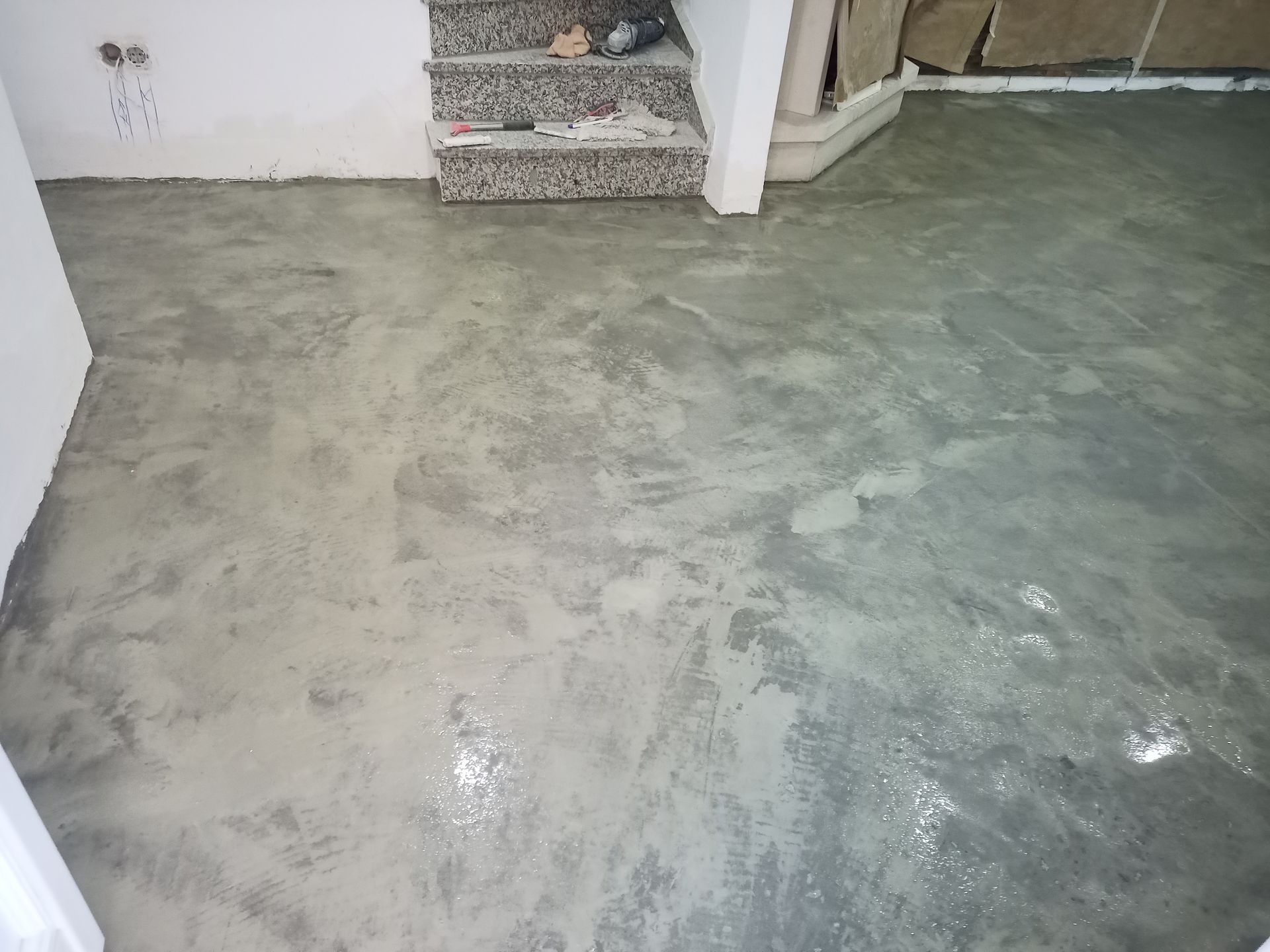 Piso de concreto em construção, cinza com superfície texturizada, próximo à escada.
