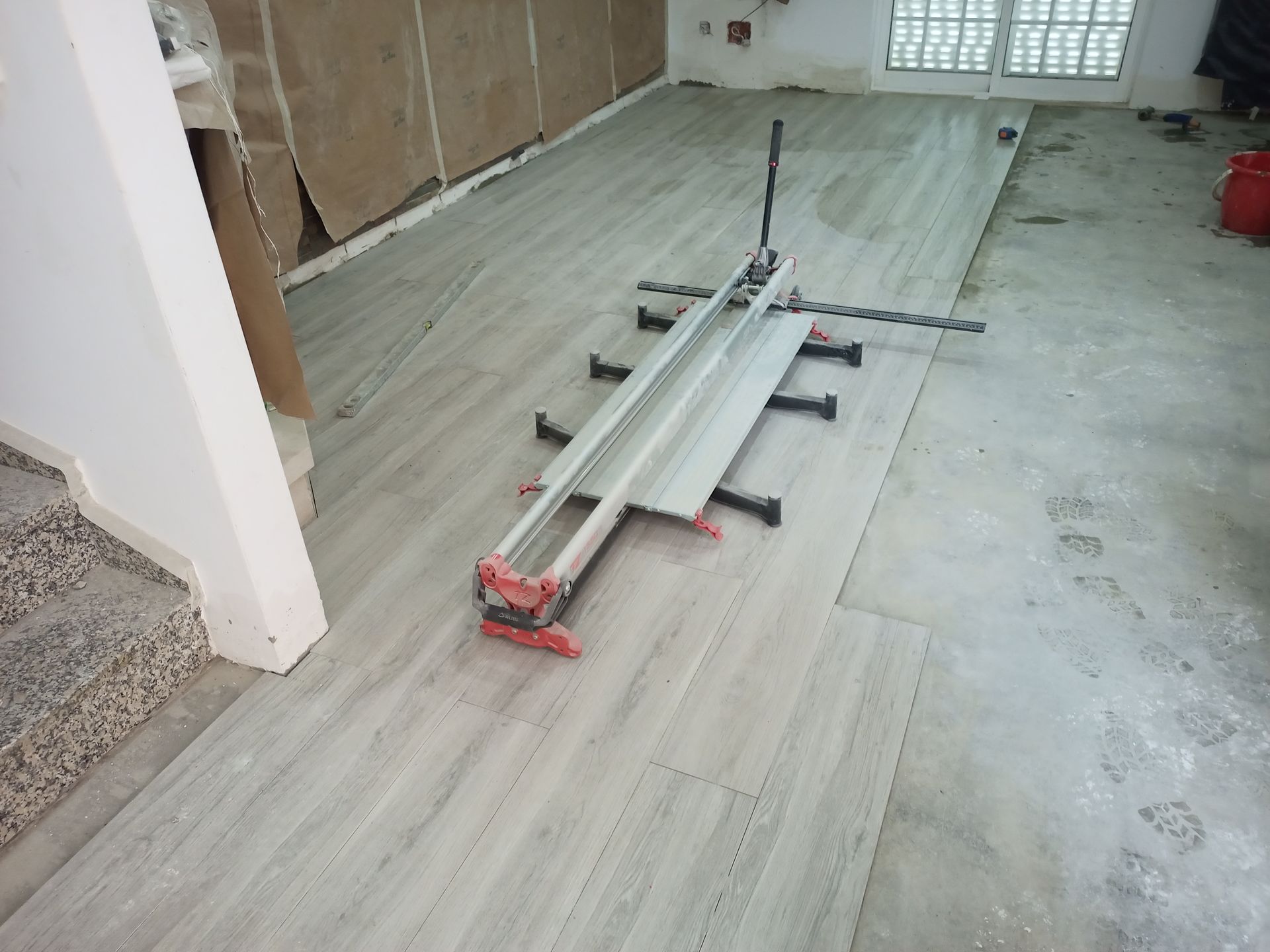 Cortador de azulejos cortando um azulejo cinza claro em um piso de concreto em uma sala em construção.