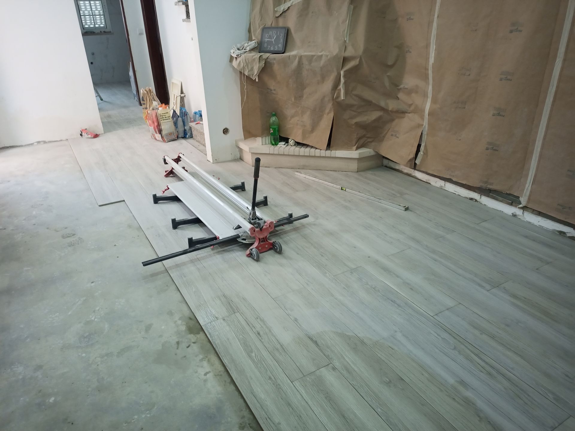 Cortador de azulejos em pisos imitando madeira recém-instalados em um cômodo em construção.