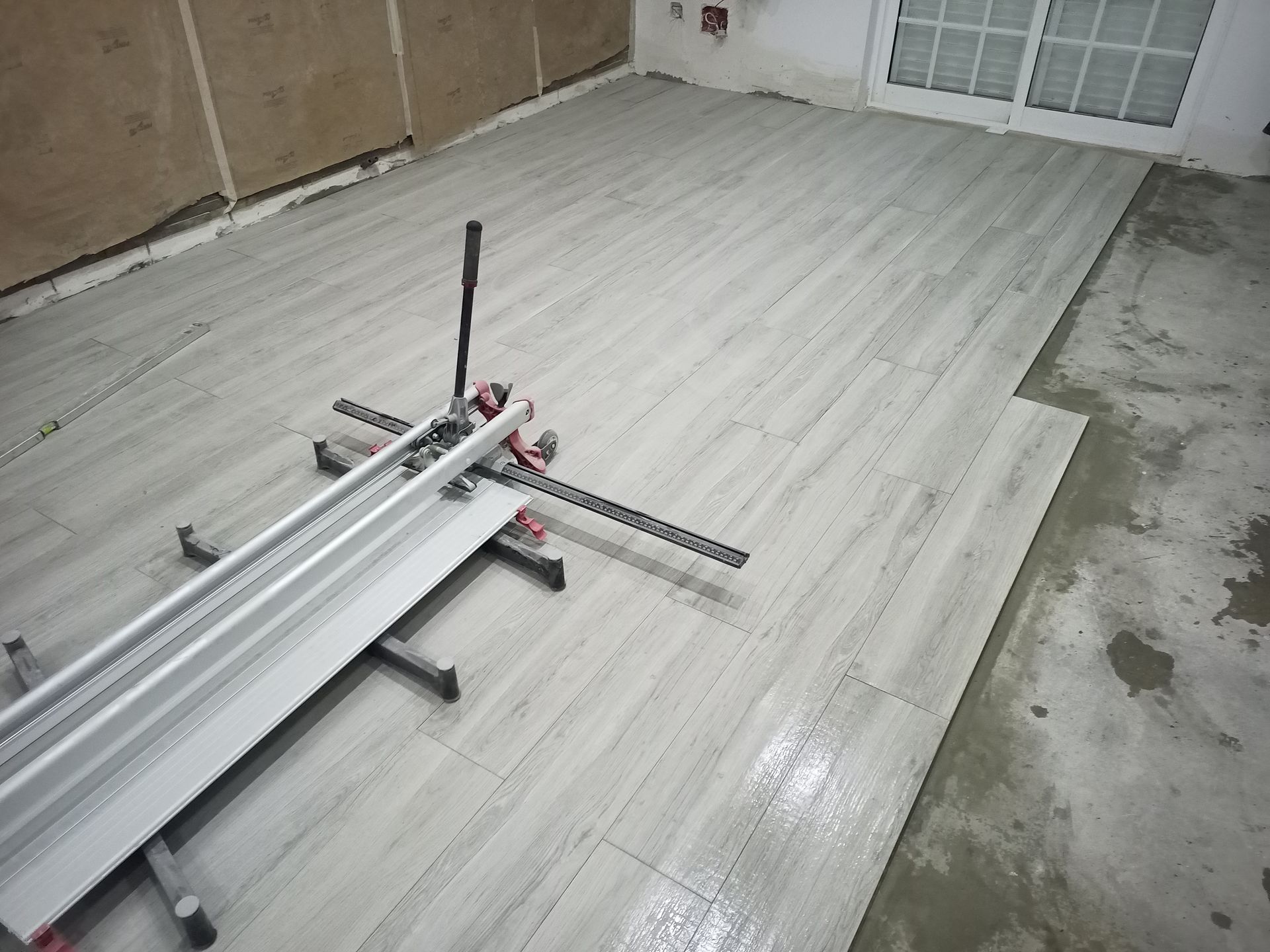 Cortador de azulejos em um piso parcialmente revestido com ladrilhos retangulares cinza-claro em um cômodo.