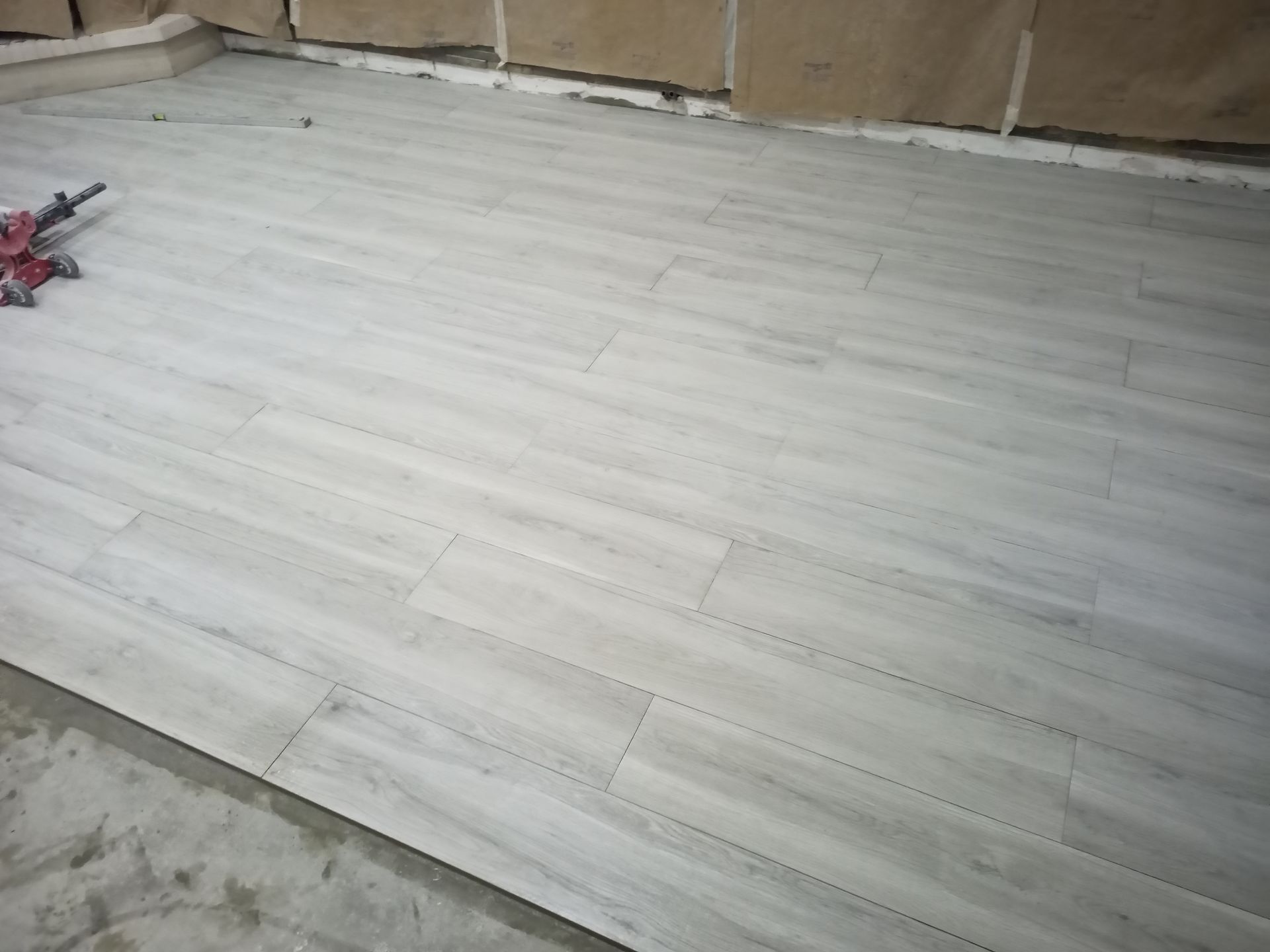 Piso imitando madeira em tom cinza claro sendo instalado em um cômodo com paredes inacabadas.