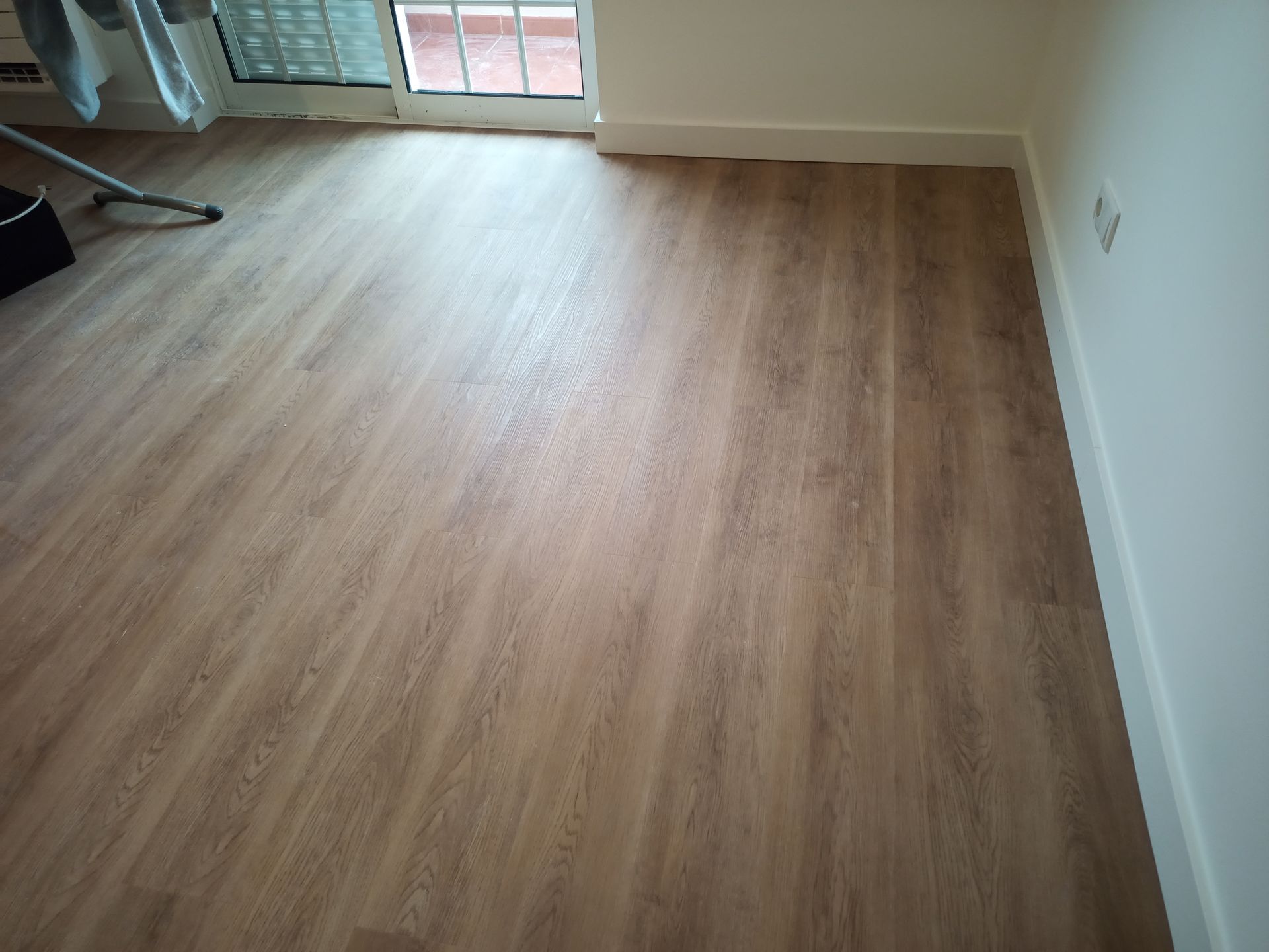 Piso imitando madeira em tom castanho claro em um cômodo com paredes e rodapés brancos.