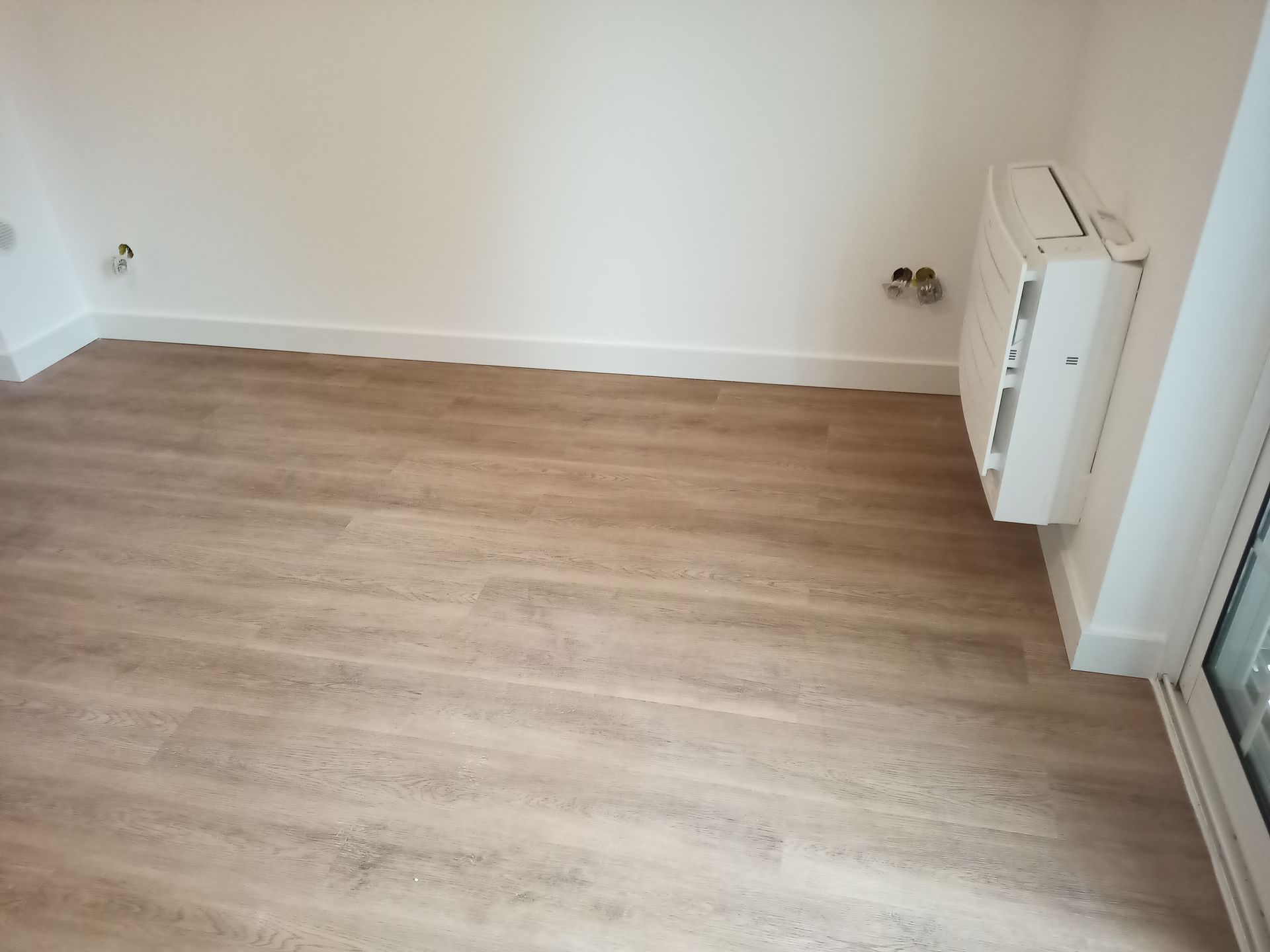 Quarto vazio com piso imitando madeira e paredes brancas. Há um aparelho de ar condicionado na parede.