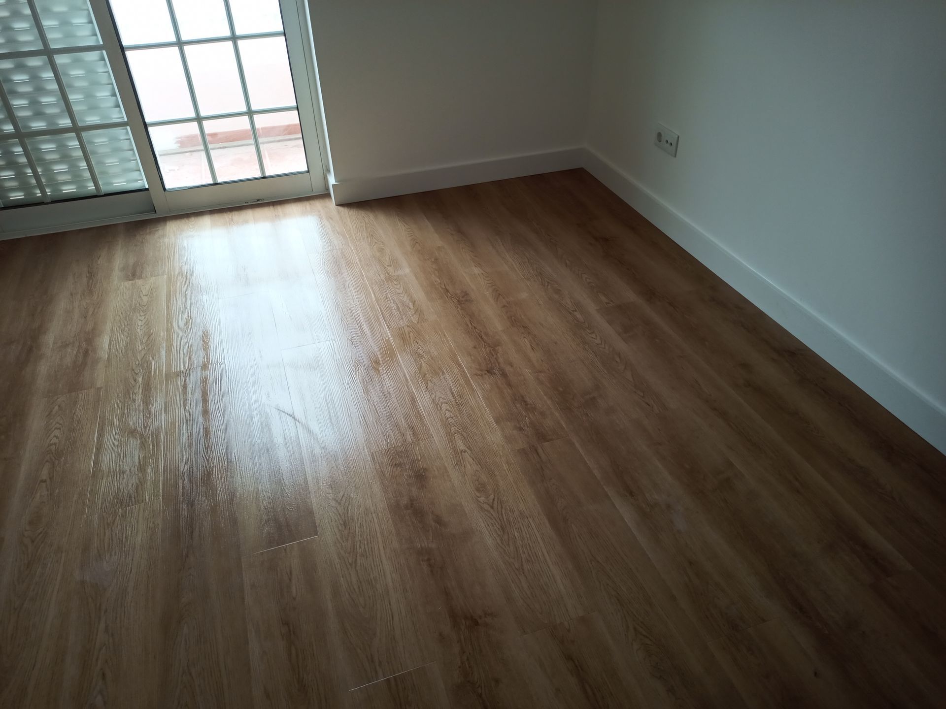 Piso de madeira com rodapés brancos e porta de vidro deslizante.