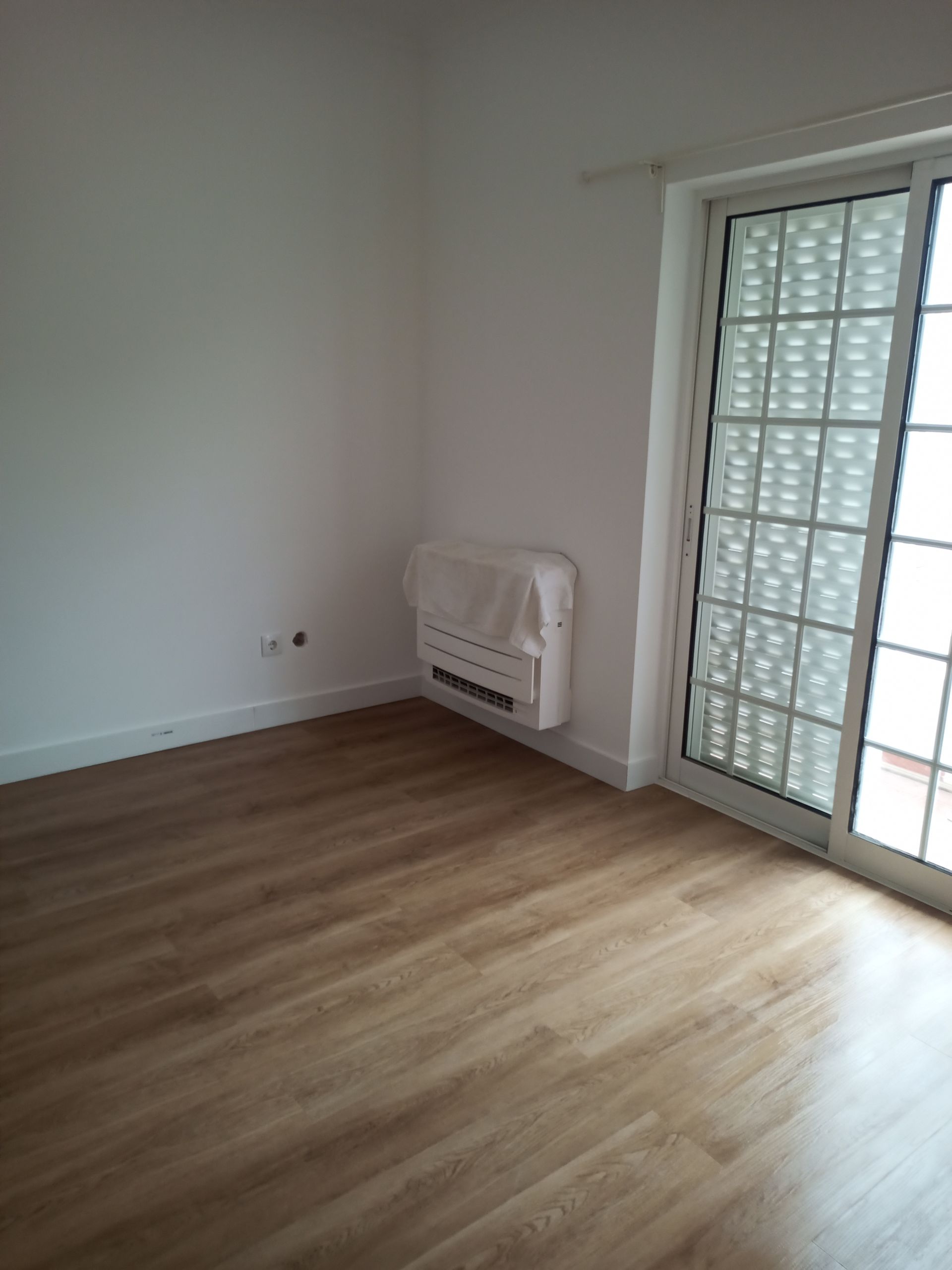 Quarto vazio com piso imitando madeira, paredes brancas e porta de vidro deslizante com janela padronizada para maior privacidade.