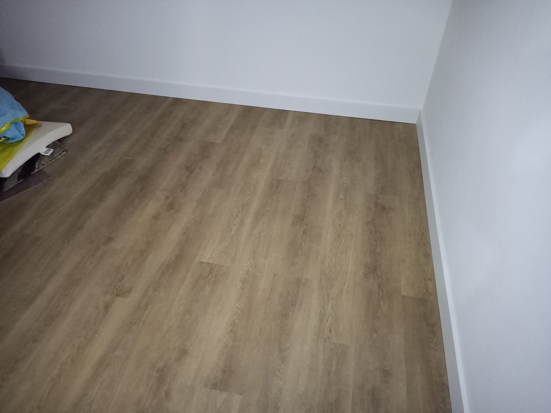 Piso de madeira em um quarto com paredes e rodapés brancos.