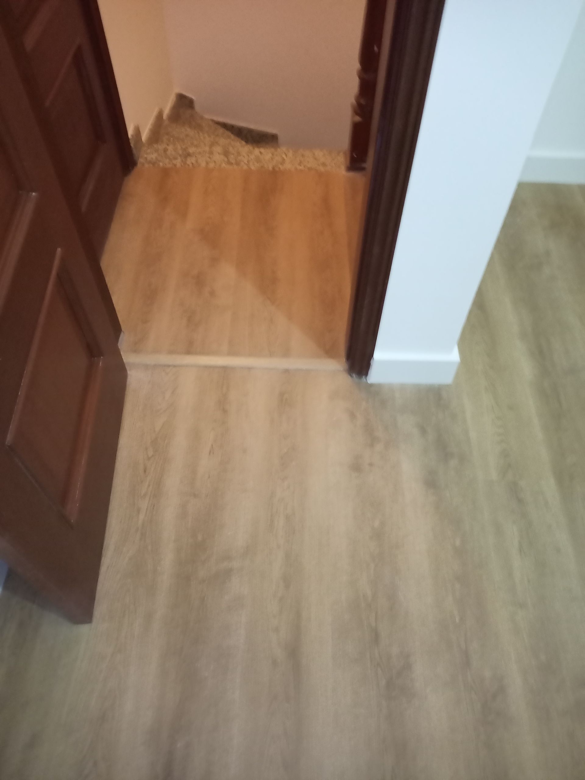 Piso de madeira e porta de acesso à escada. Paredes bege e porta marrom.