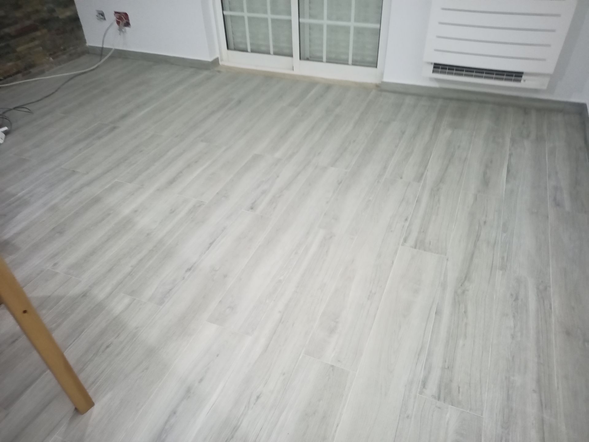 Piso imitando madeira em tom cinza claro em um cômodo com janela e aquecedor.