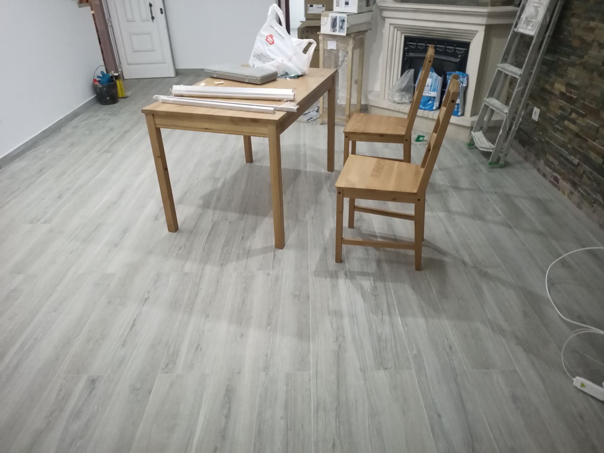 Uma mesa de madeira e duas cadeiras sobre um piso de madeira cinza claro em uma sala.