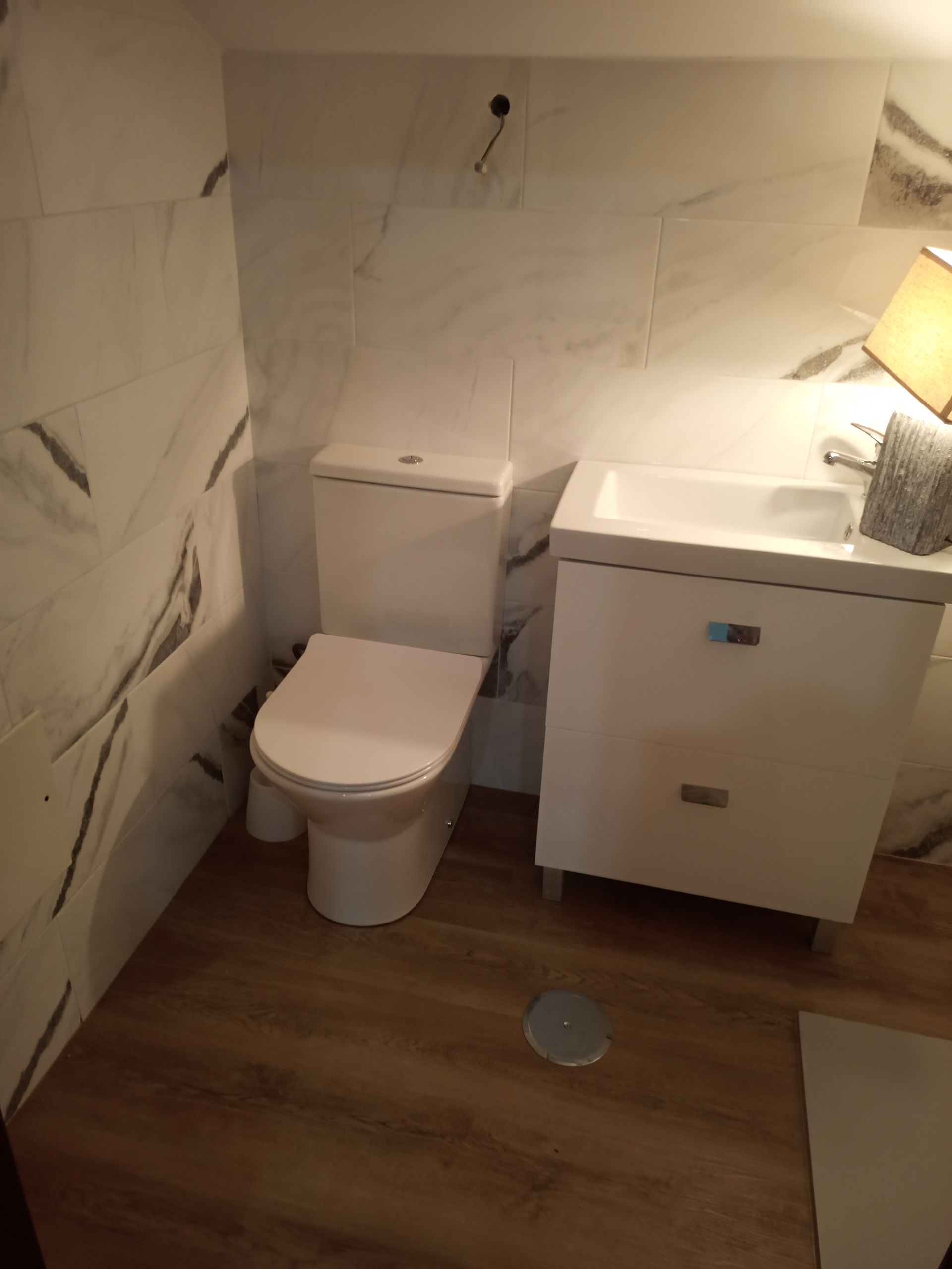 Banheiro branco com vaso sanitário, pia e piso imitando madeira.