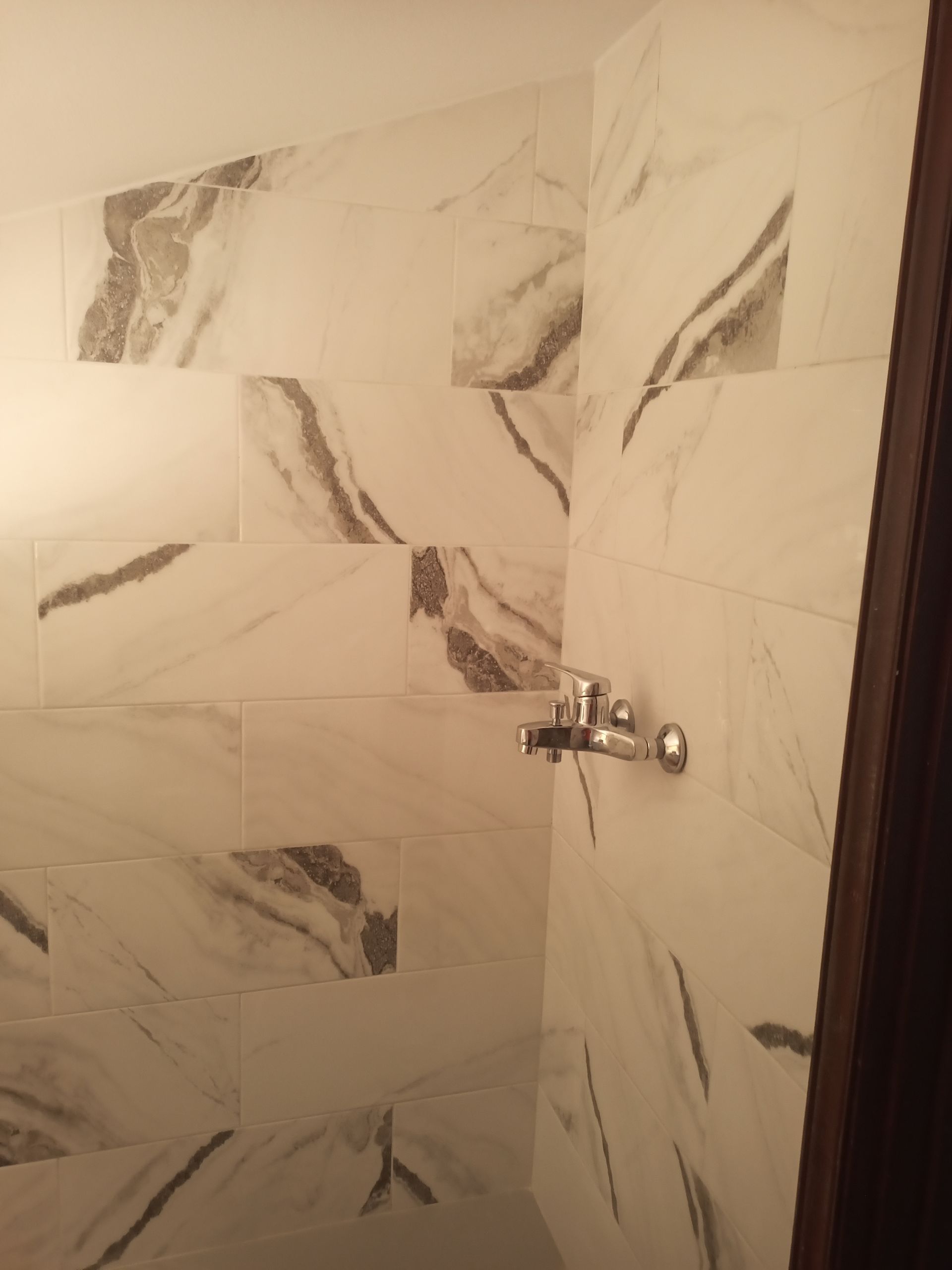Azulejos de chuveiro com padrão de mármore branco e torneira prateada. Vista de canto.