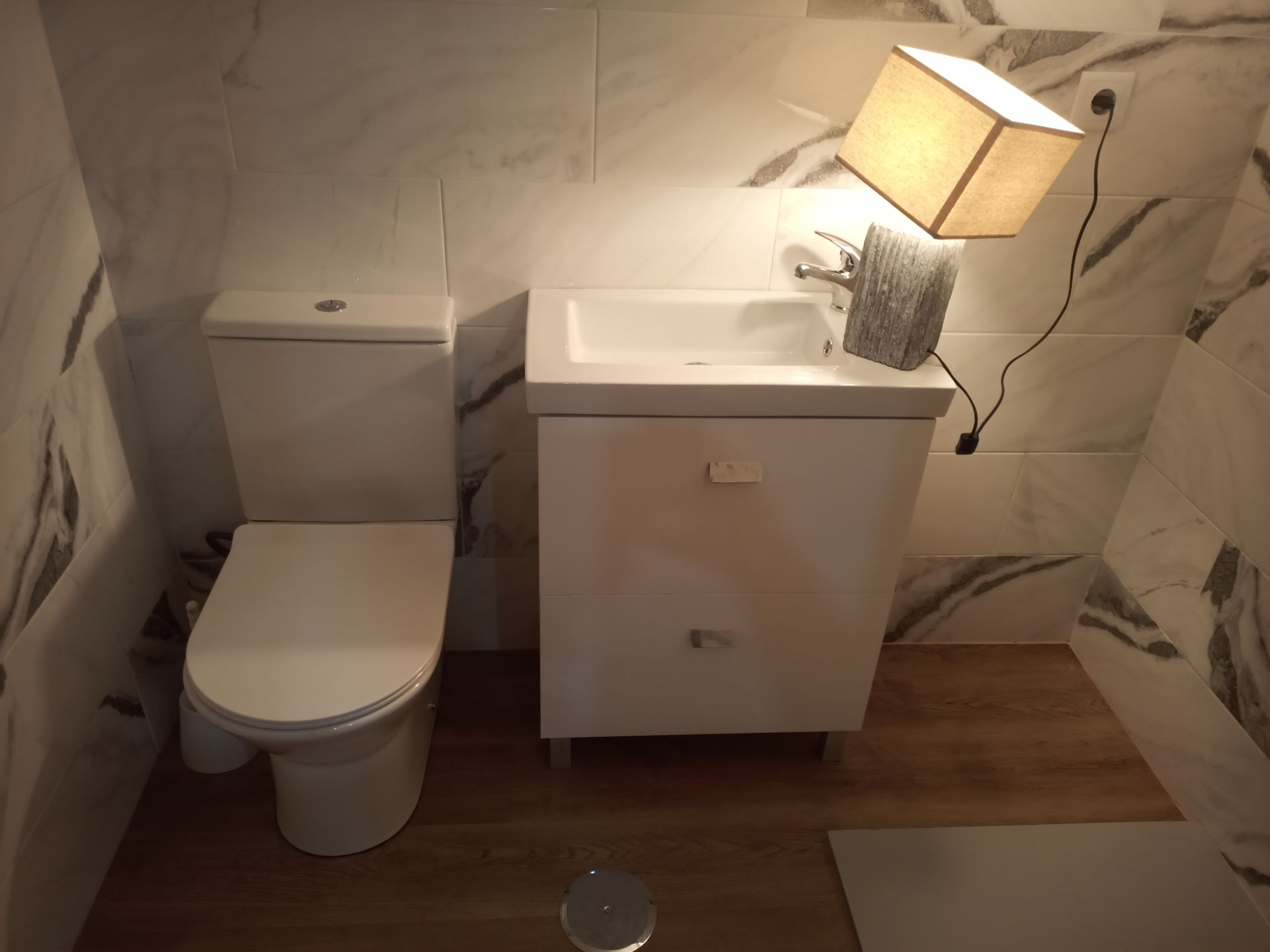 Banheiro branco com vaso sanitário, pia e luminária em forma de cubo.