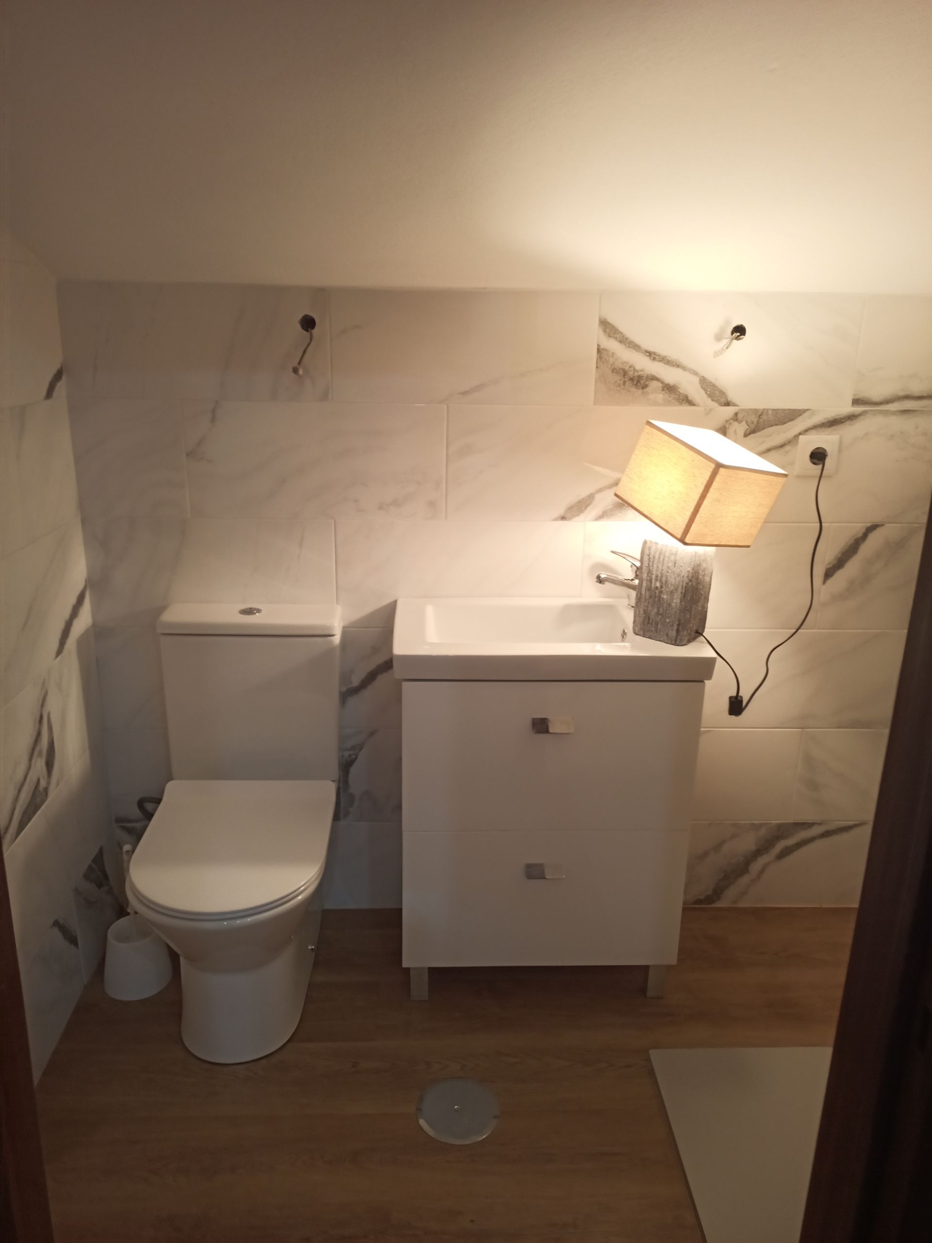 Banheiro com vaso sanitário branco, pia e paredes com estampa de mármore. Há também um lustre.