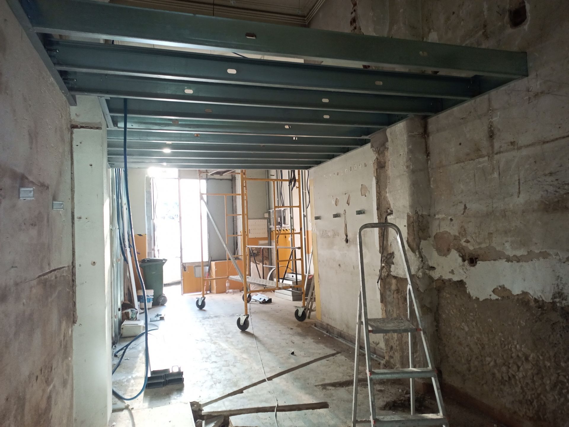 Canteiro de obras. Vigas de aço instaladas no teto. Paredes nuas, porta que dá para o exterior.