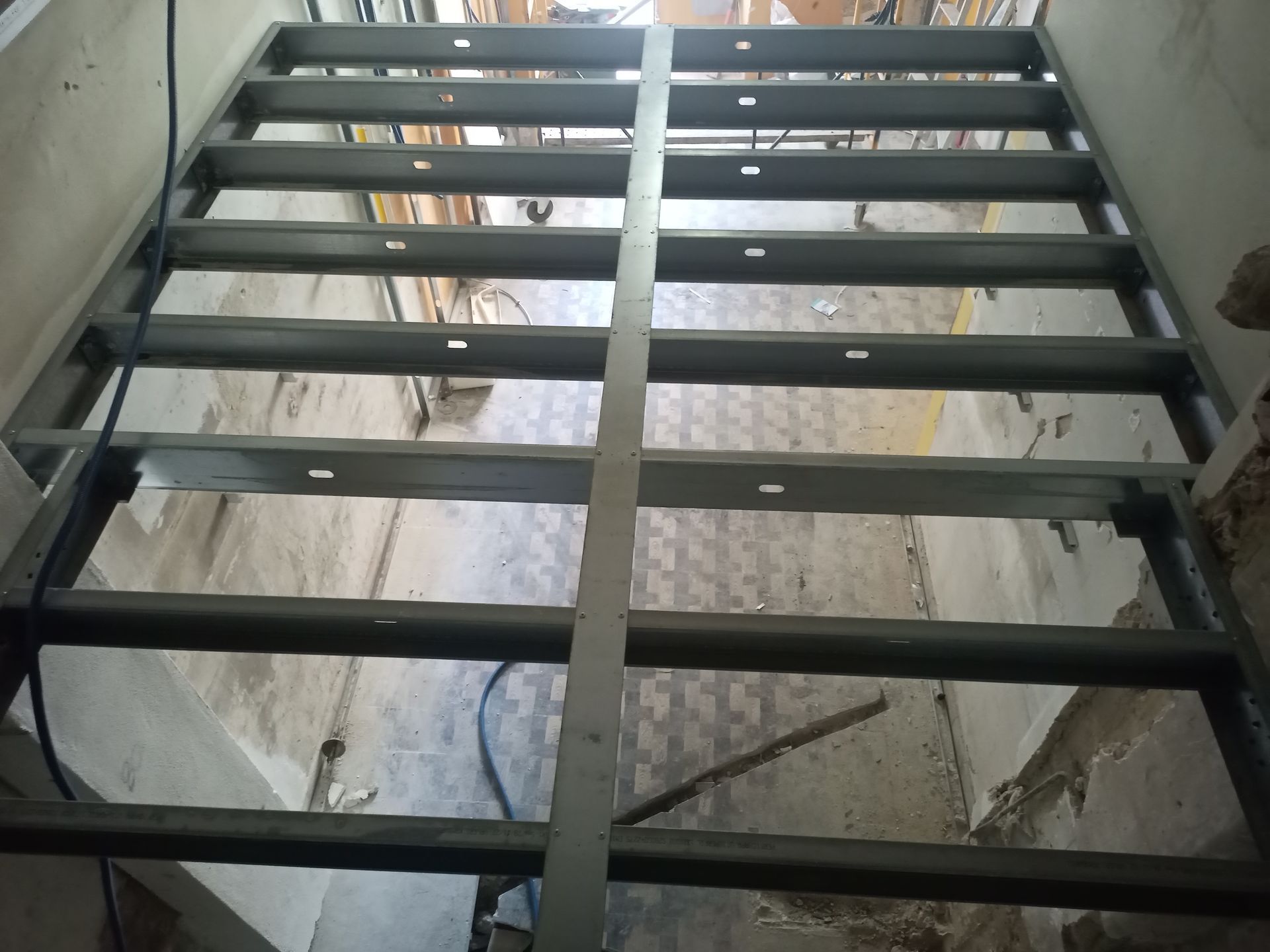 Estrutura metálica para piso, vista de cima, em uma sala com paredes e teto danificados.